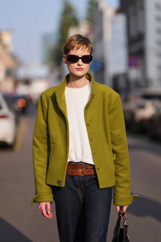 Frau trägt weißes Shirt unter senfgelber Jacke, kombiniert mit Jeanshose und Multi-Belt-Layering