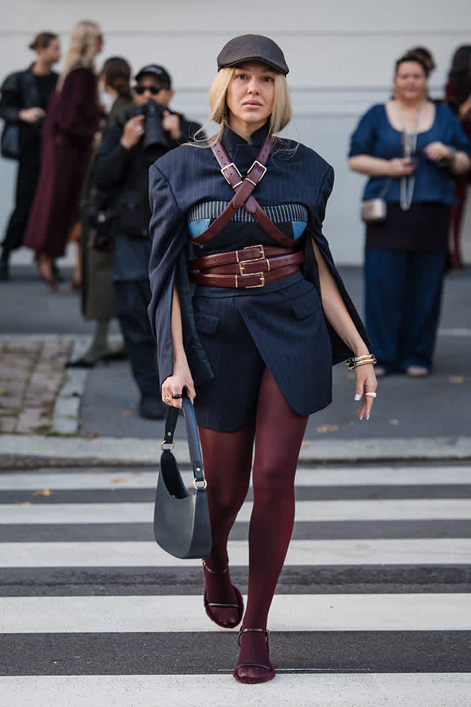 Frau trägt blauen Cape-Blazer mit Gürtel-Harness und roter Strumpfhose