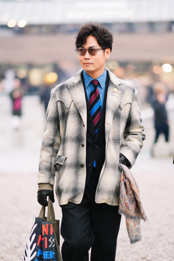 Mann auf der Pitti Uomo 2026, trägt grauen Mantel mit Nadelstreifenhose und Handschuhen