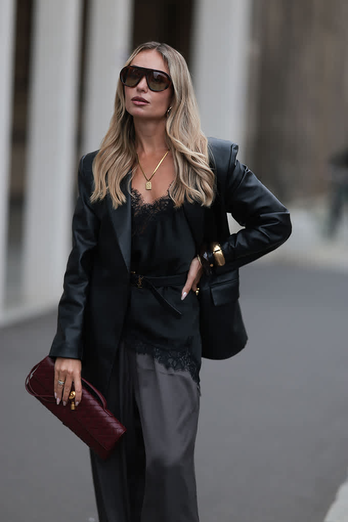 Frau zeigt edgy Outfit: Schwarzes Camisole, schwarzer Blazer und dunkle Hose gestalten einen Ton-in-Ton-Look
