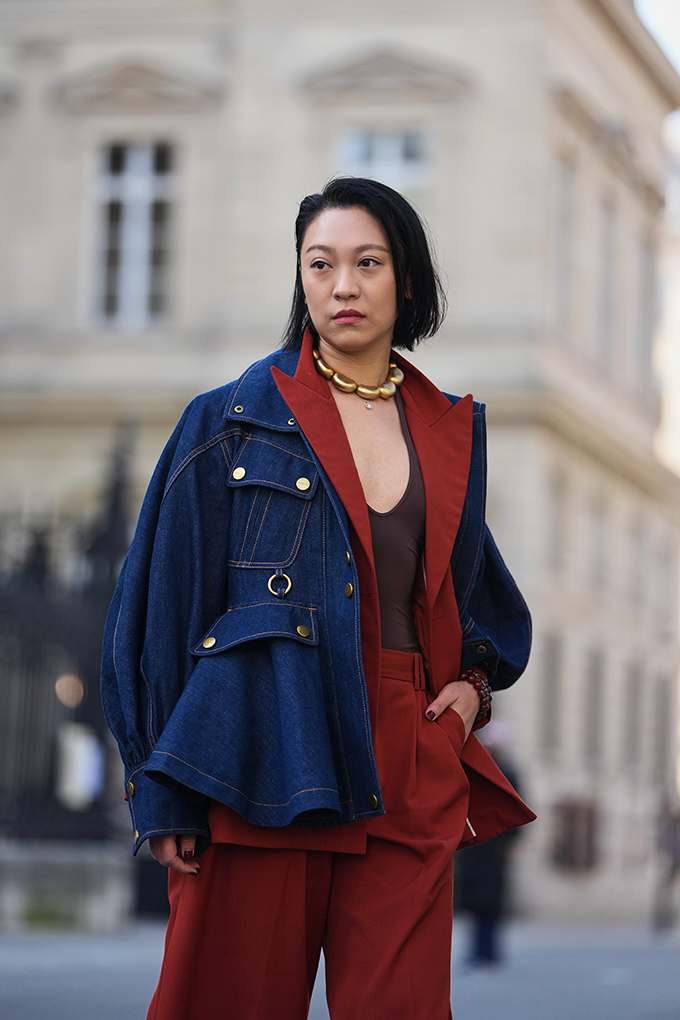 Frau trägt dunkelblaue Denim-Jacke über rostrotem Anzug mit Goldkette