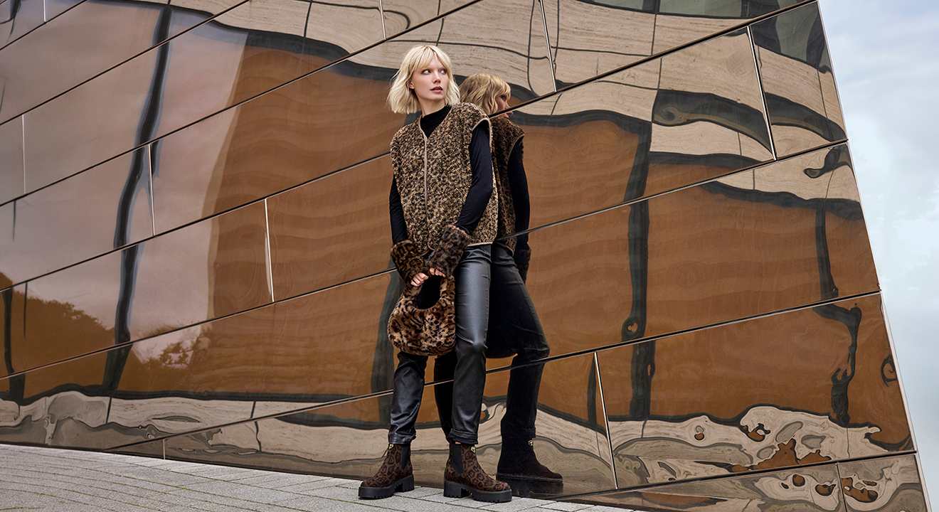 Frau trägt Animal-Print Teddy-Weste über schwarzem Rollkragen, kombiniert mit Leder-Pants, Fell-Bag im Leo-Look und Plateau-Boots