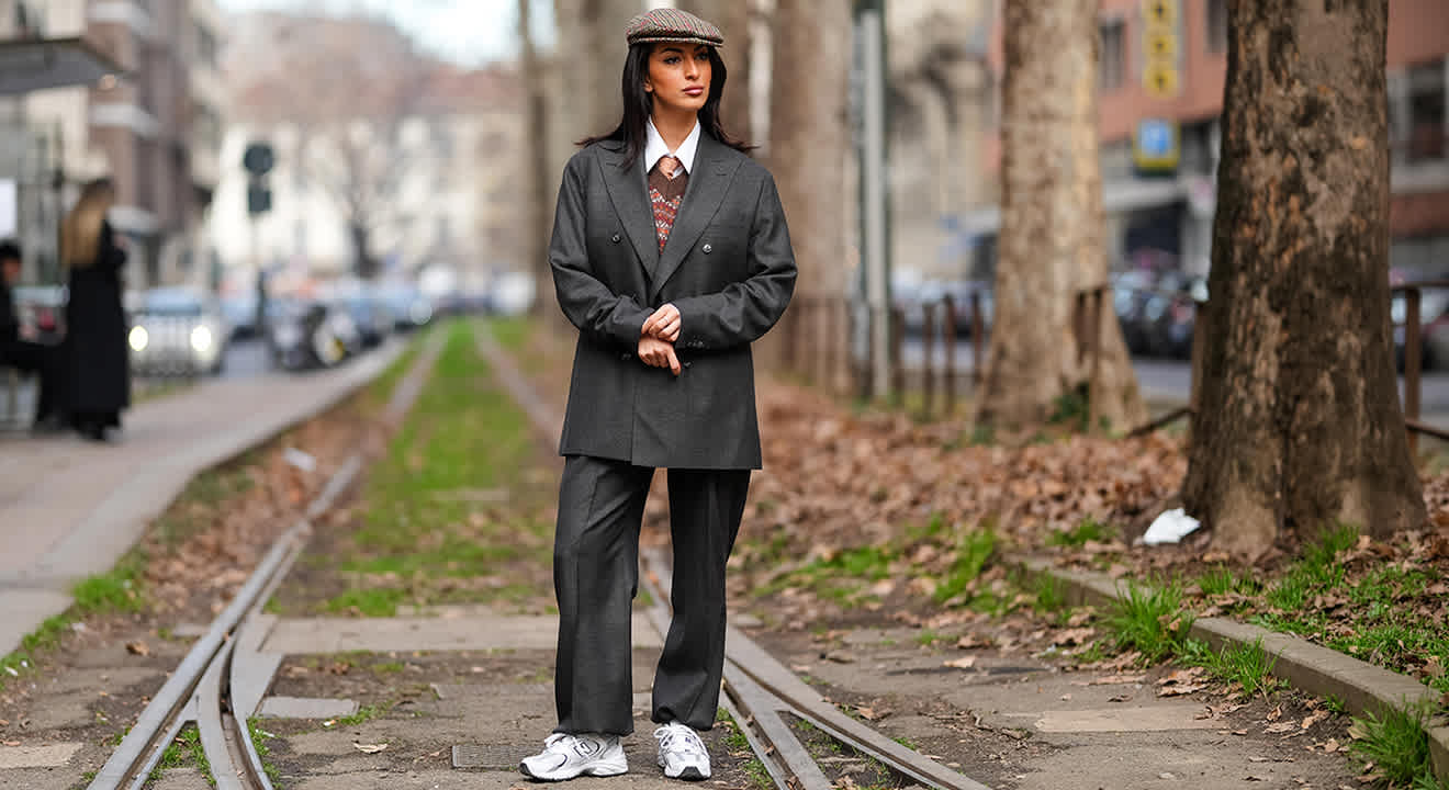 Streetstyle-Look mit grauem Oversize-Anzug, Schiebermütze und weißen New Balance-Sneakern auf Straßenbahngleisen