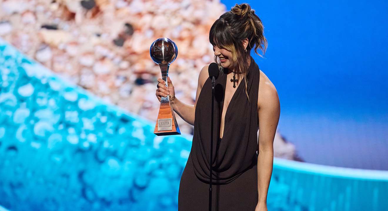 Frau im schwarzen Abendkleid hält Trophäe bei Preisverleihung am Mikrofon