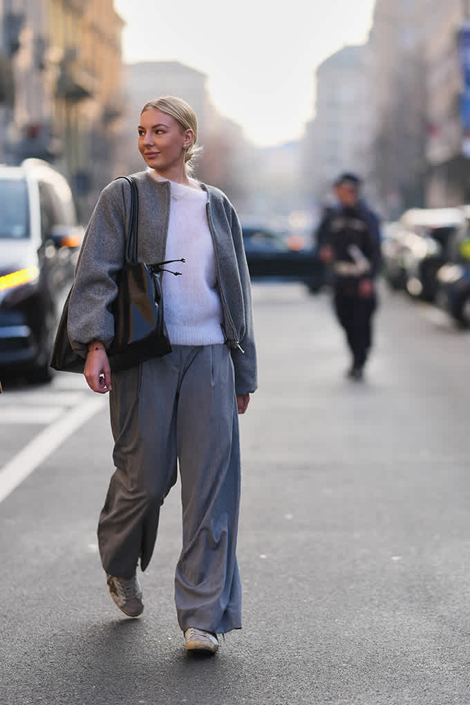 Frau in weißem Strickpullover, grauem Mantel und weiter grauer Hose