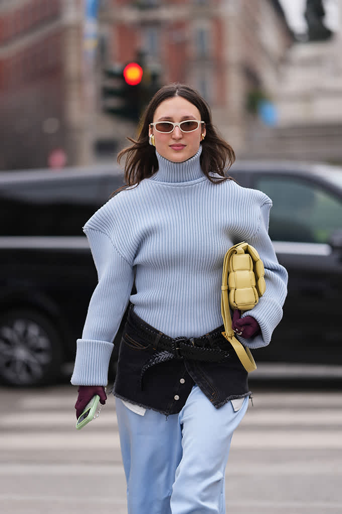 Frau mit hellblauem Rollkragenpullover, schwarzer Shorts und weißer Sonnenbrille