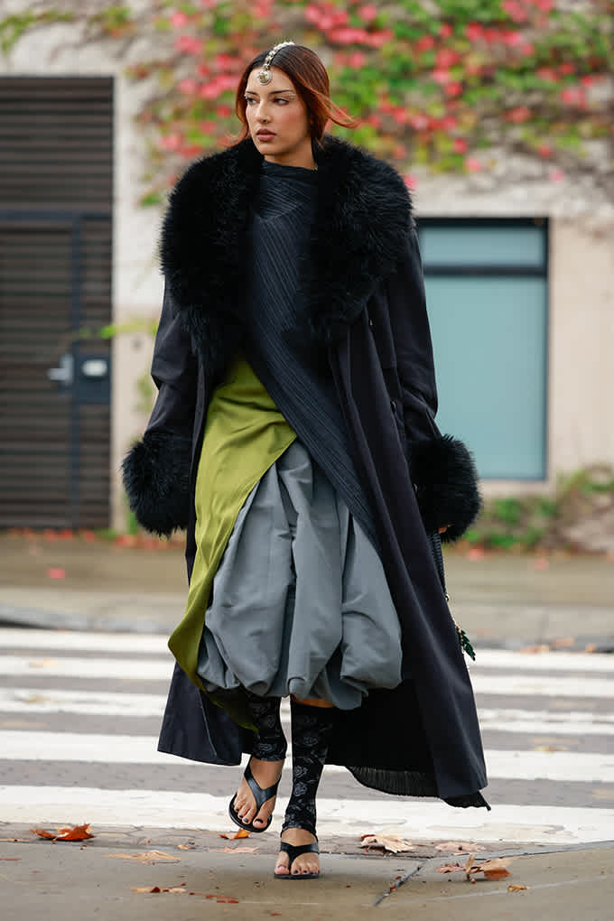 Boho Chic-Winterlook mit schwarzem Mantel mit Fellbesatz, Ballonrock und Sandalen auf Zebrastreifen