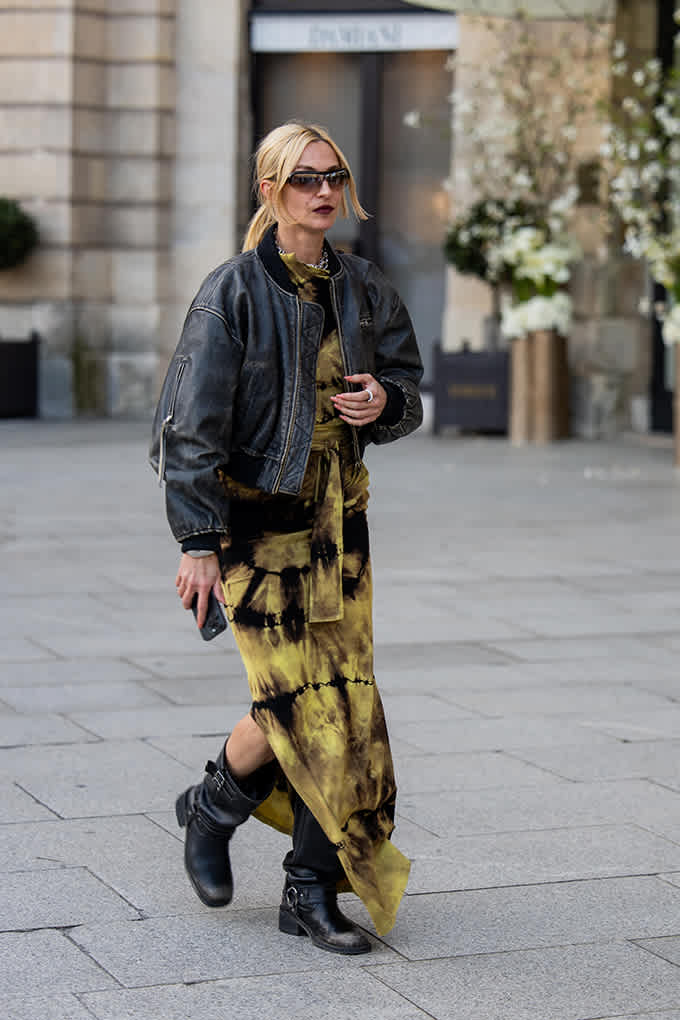 Frau in einem schwarz-olivfarbenen Batik-Kleid mit fleckigem Tie Dye Muster, kombiniert mit Lederjacke und Boots