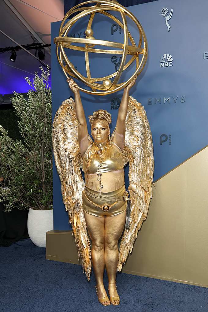 Megan Stalter posiert als goldene Emmy-Statue mit Flügeln und einer großen Emmy-Kugel über dem Kopf