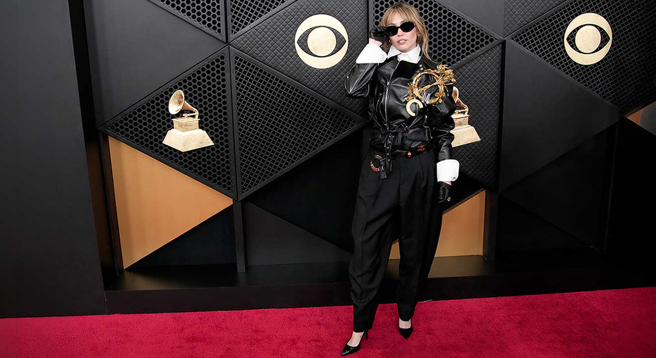 Sängerin Miley Cyrus mit Grammy auf dem roten Teppich in schwarzer Lederjacke, Anzughose und spitzen Pumps