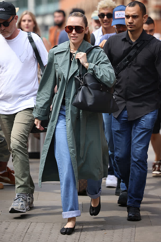 Miley Cyrus im olivgrünen Trenchcoat und Mom-Jeans mit Umschlag, trägt schwarze Ballerinas als Streetstyle