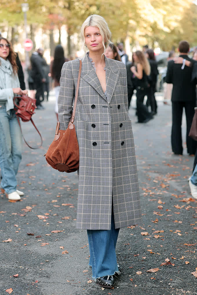 Frau im langen Glencheck-Mantel und Wide-Leg-Jeans trägt Nieten-Loafer und braune Wildledertasche