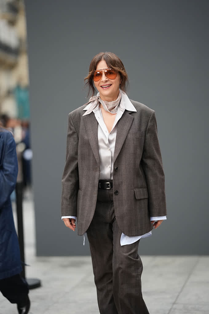 Frau im grauen Oversize-Anzug mit Satinbluse, Halstuch und getönter Pilotenbrille im Soft Tailoring-Look