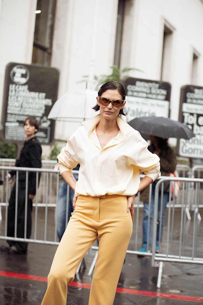 Frau in cremefarbener Oversize-Bluse und gelber High-Waist-Hose mit getönter Sonnenbrille im Streetstyle