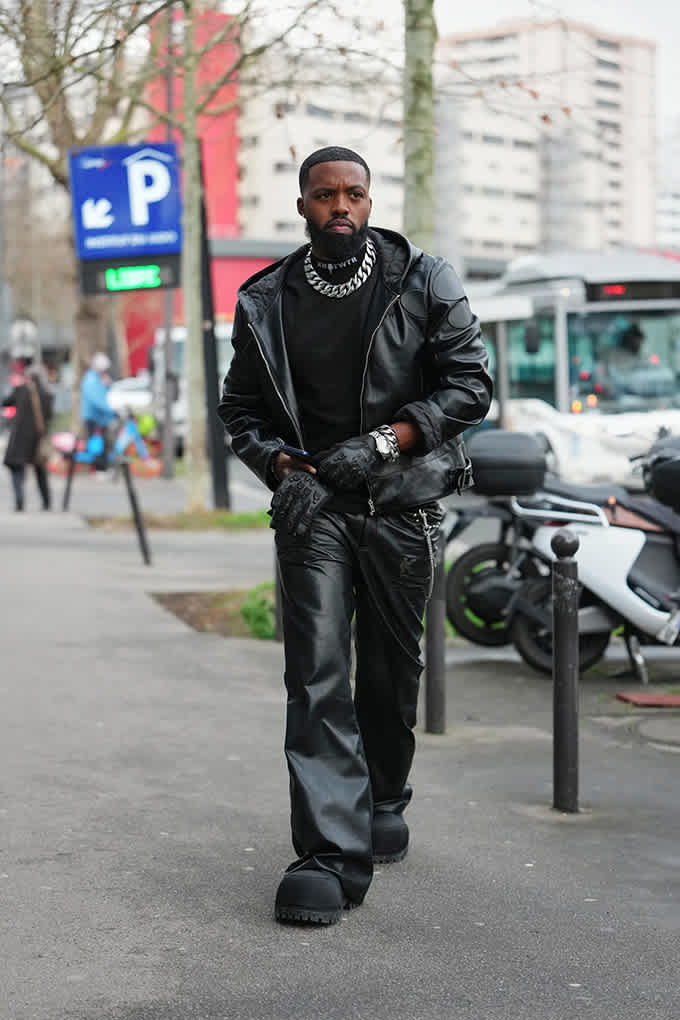 Mann im All-Black-Lederlook mit Bikerjacke und Gliederkette trägt Boots mit grober Profilsohle im Techwear-Look