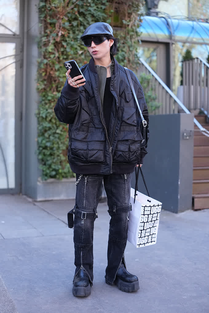 Person in schwarzer Utility-Jacke mit Taschen und Cargo-Jeans trägt Plateau-Boots und Lederschiebermütze
