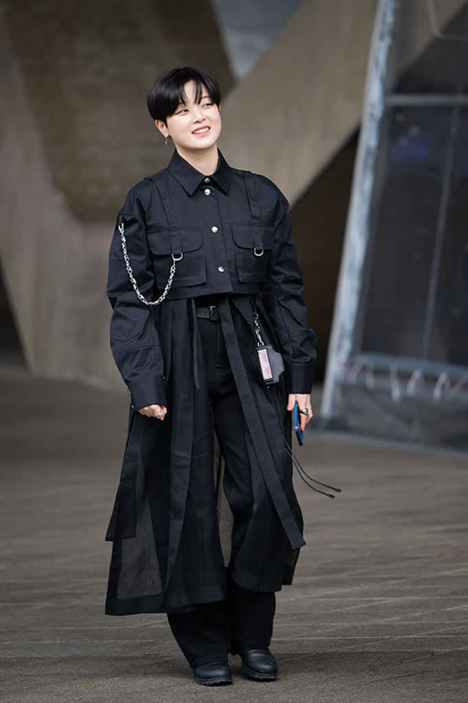 Person im schwarzen Layering-Look mit Utility-Jacke, Maxirock über weiter Hose und schwarzen Boots