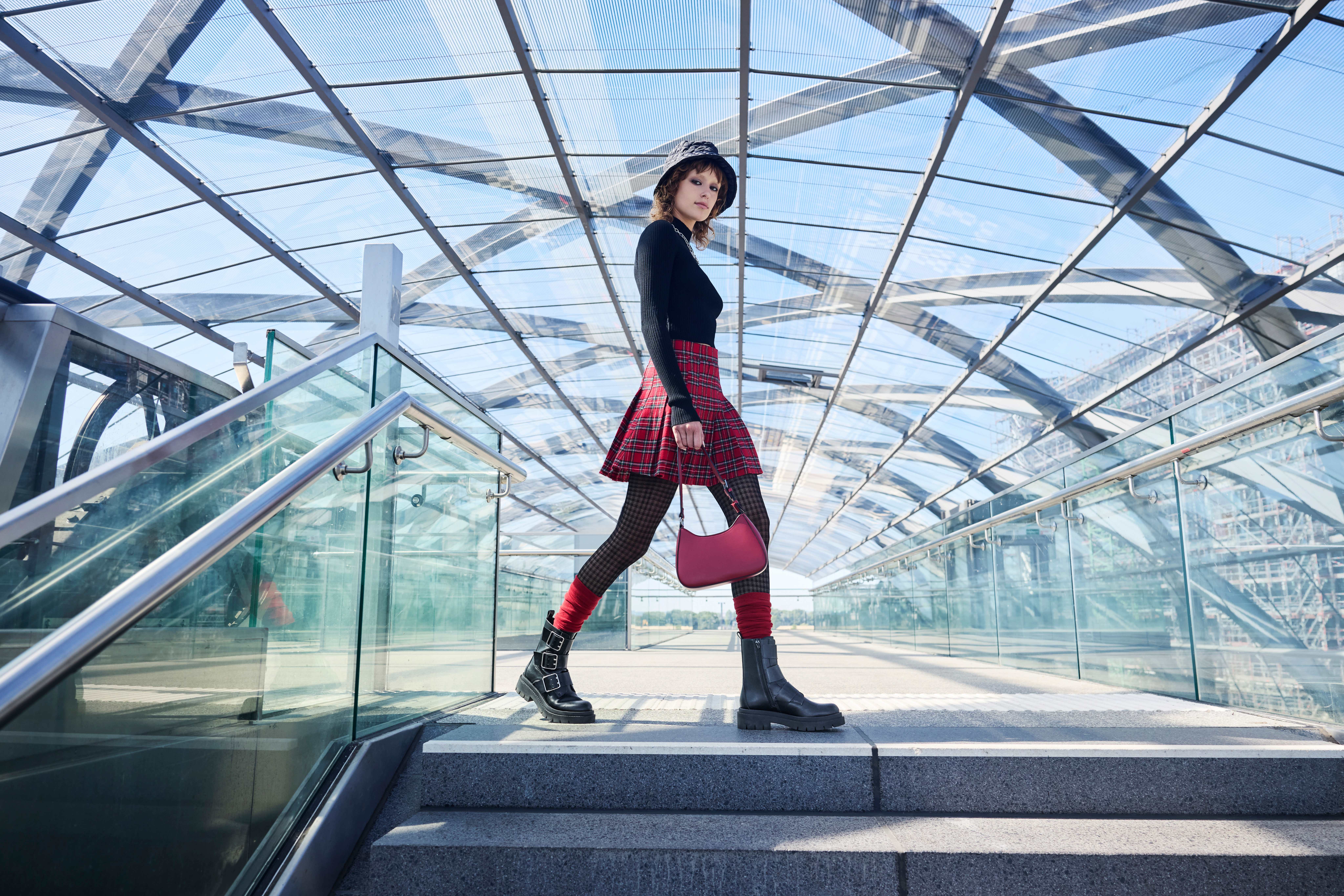 Frau in Punk Print-Outfit mit roter Handtasche am oberen Ende einer Treppe