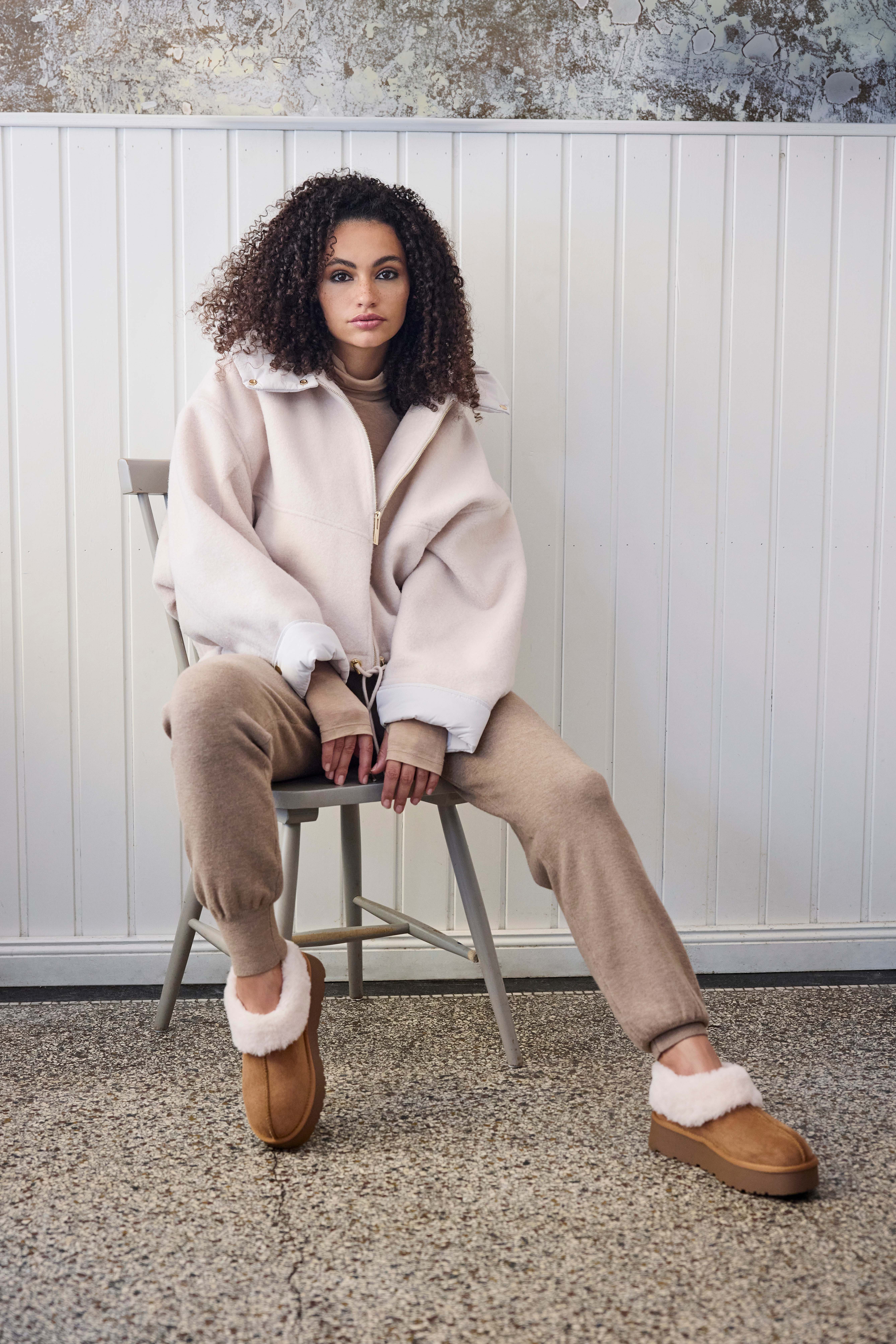 Frau mit weißem Fake Fur-Outfit, lässig sitzend auf Stuhl