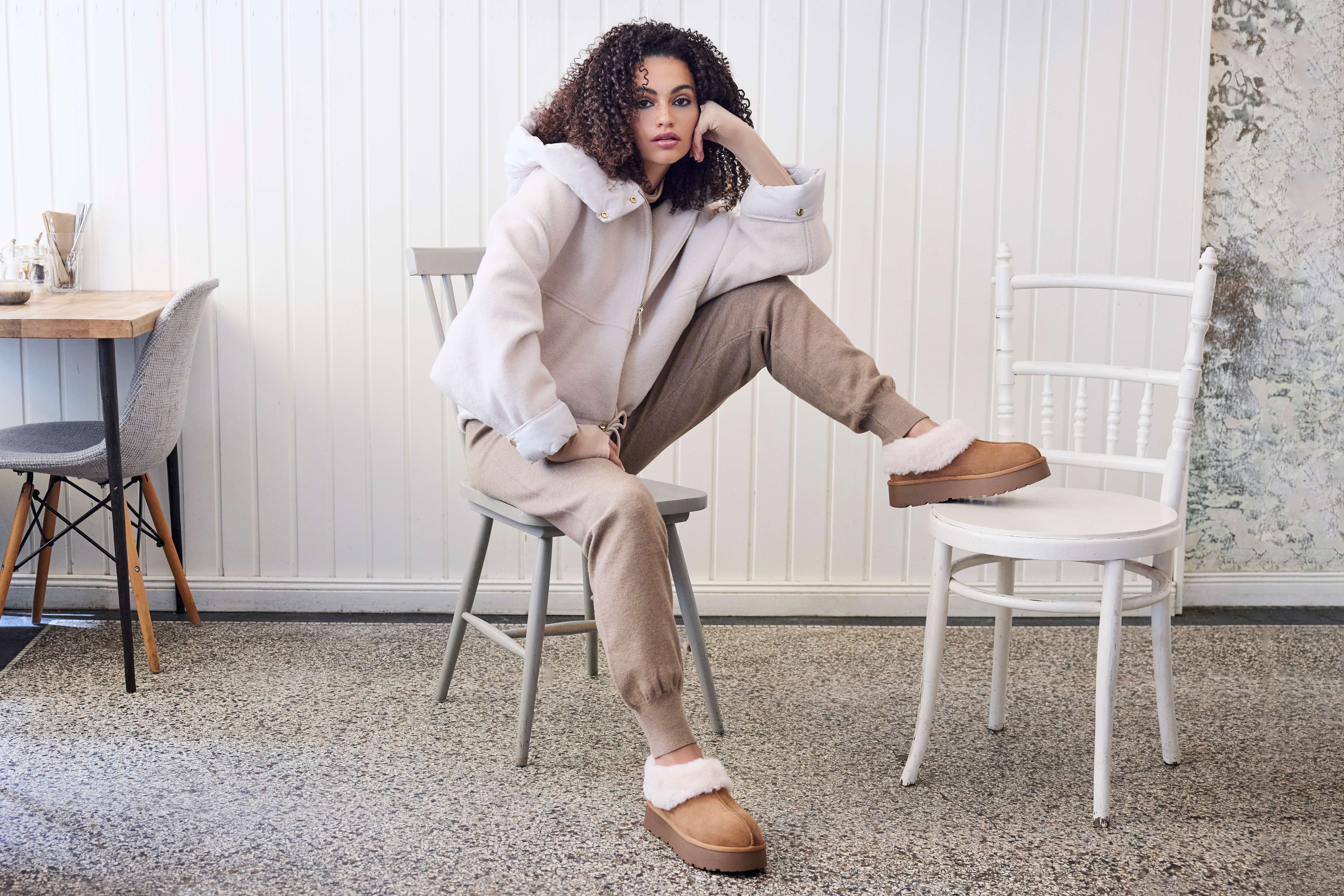 Frau mit Fake Fur-Outfit, sitzend auf Stuhl, ein Fuß aufgestützt auf weiterem Stuhl