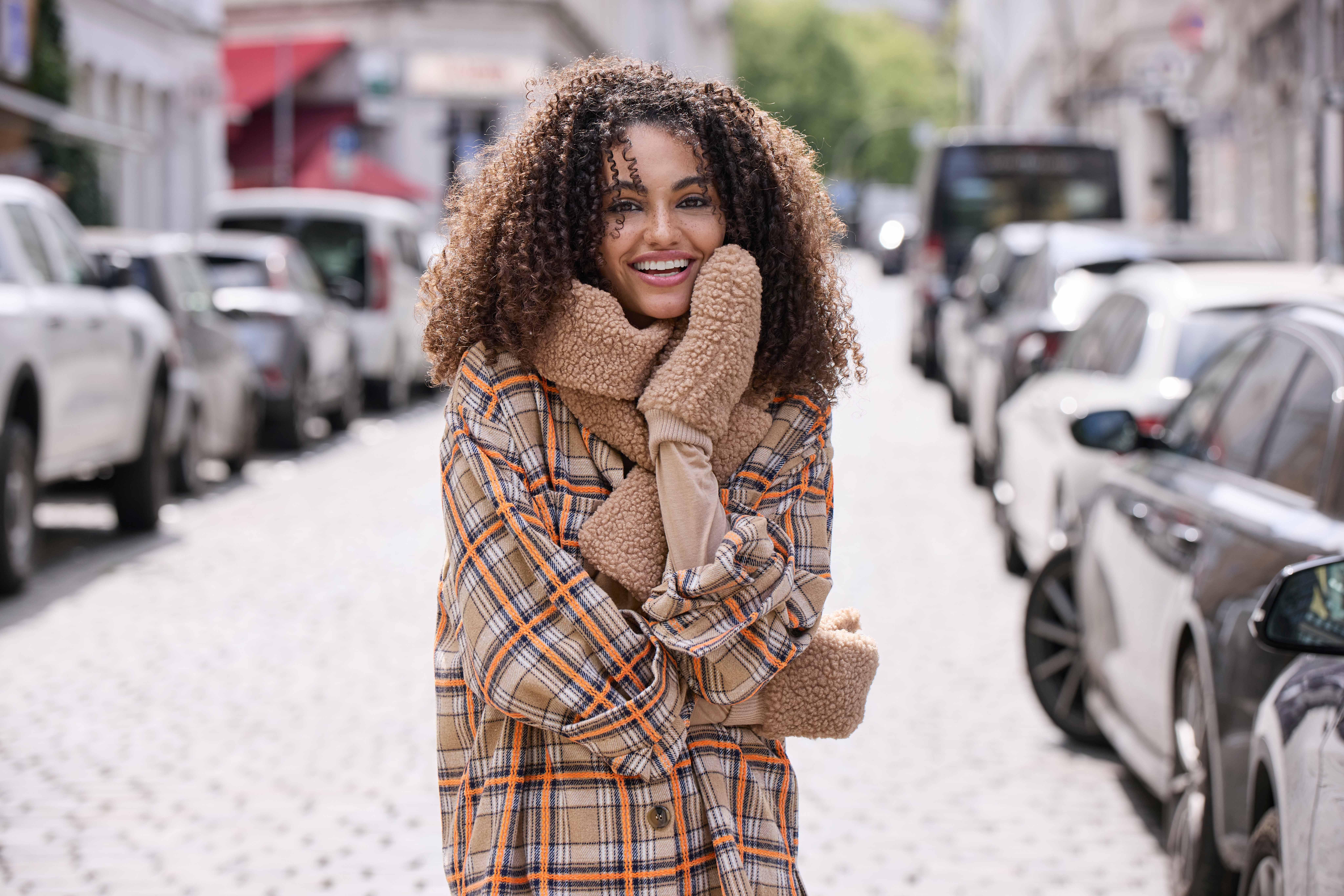 Frau mit Karo-Jacke, flauschigen Handschuhen und Schal, Blick Richtung Kamera