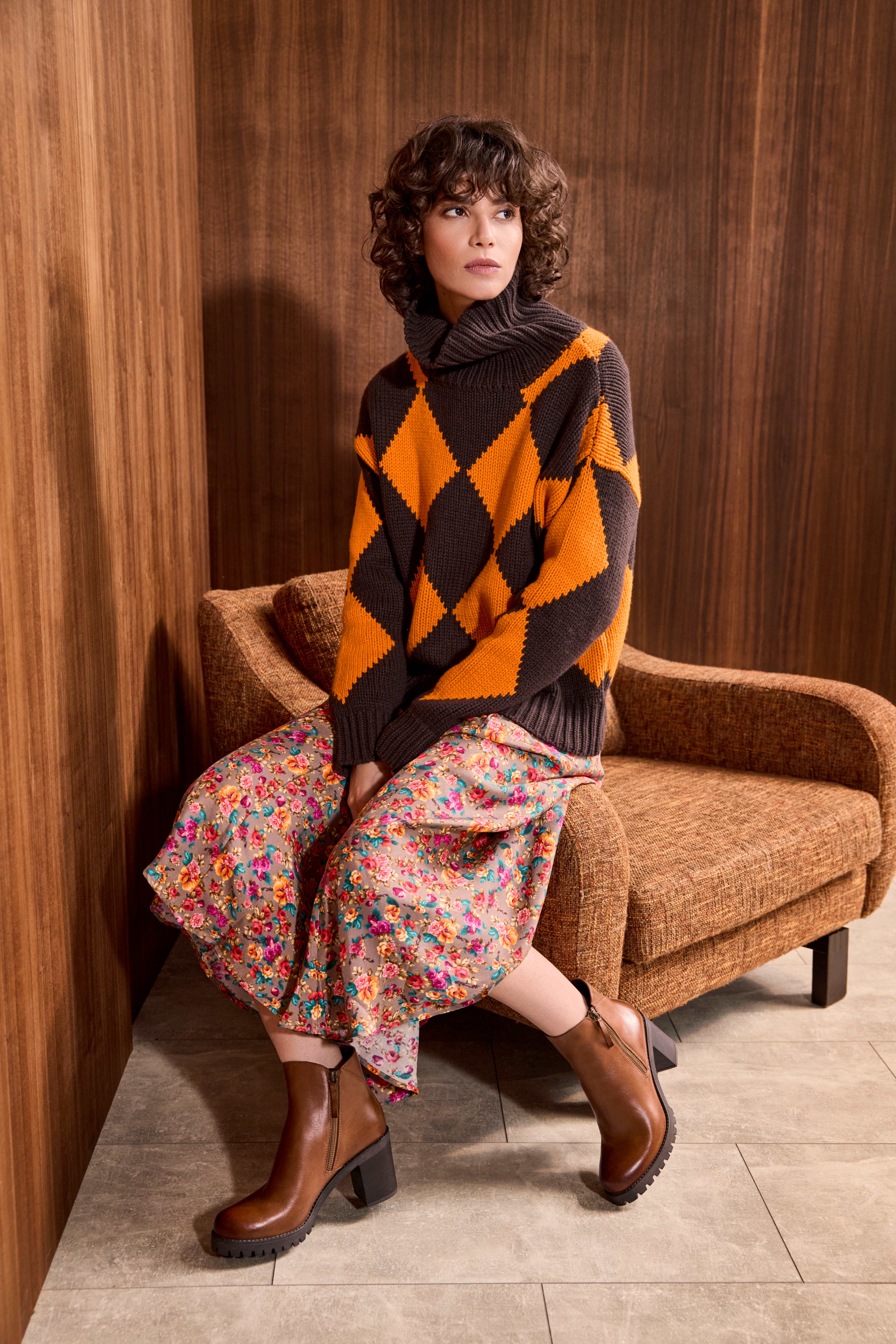 Frau in braun-orange-kariertem Pullover, trägt Blumenrock und Ankle Boots