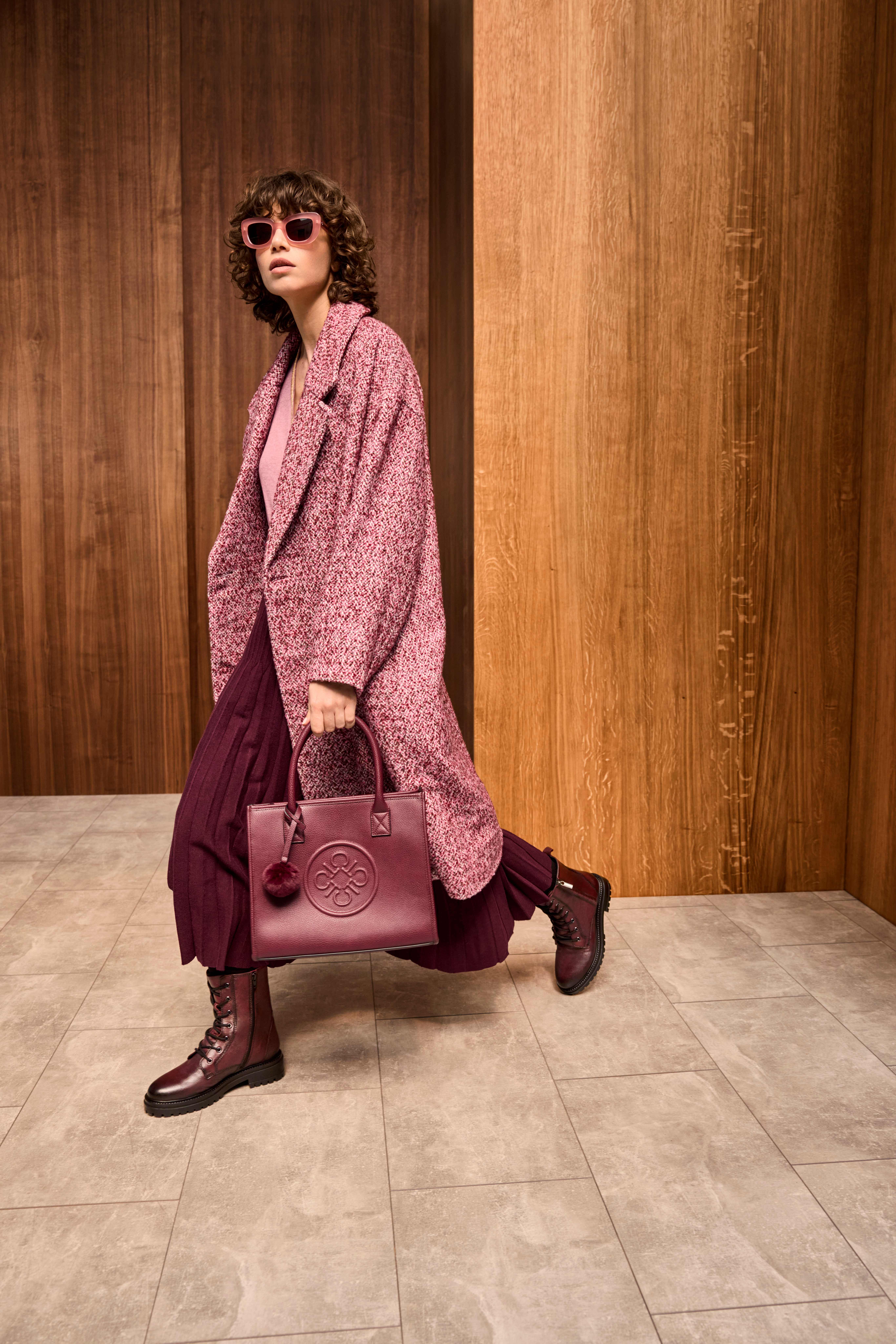 Frau spaziert mit roter Handtasche, trägt pink-rotes Jackett und Kleid, in Kombination mit Lederstiefeln