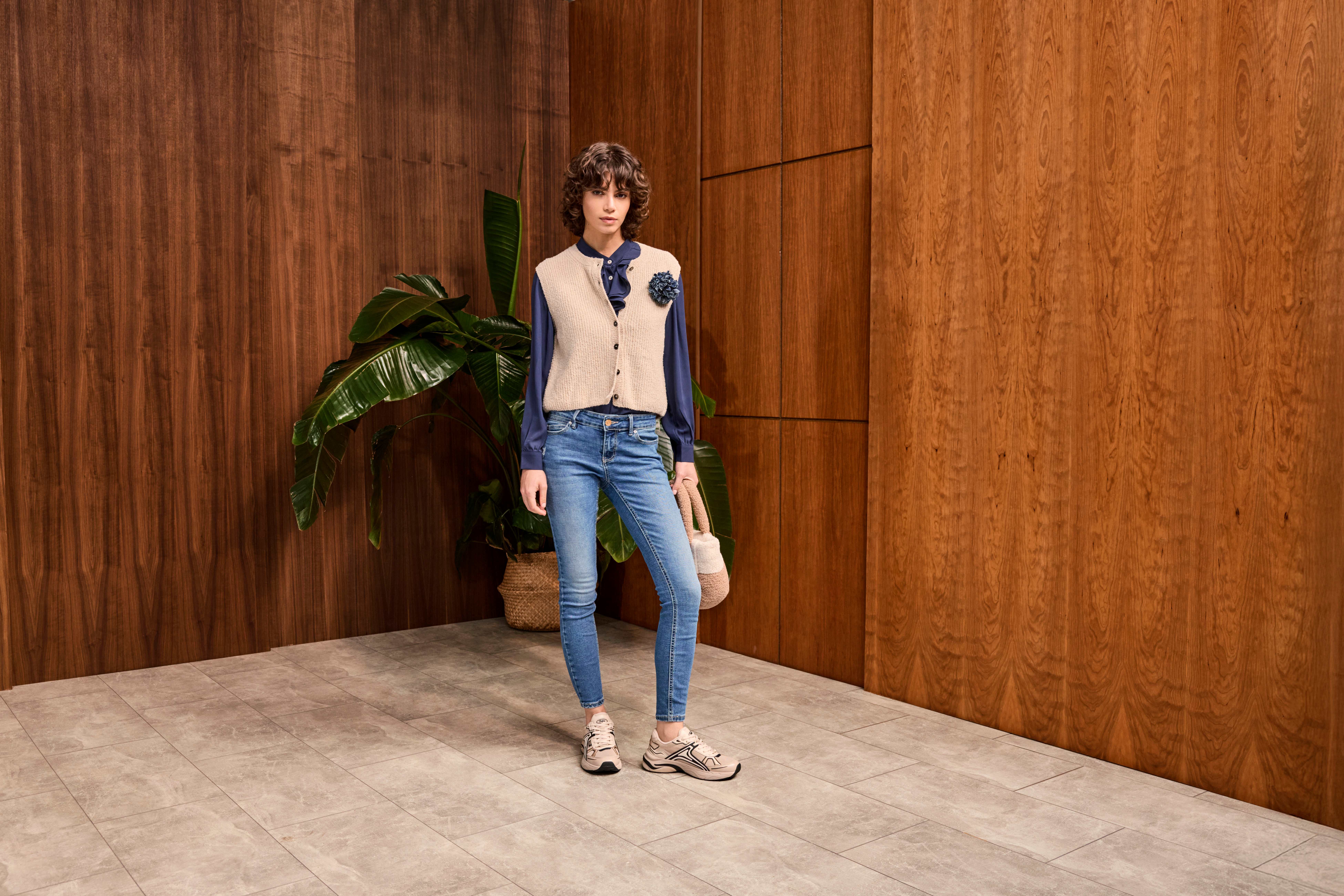 Donna con jeans blu, sneakers da papà e gilet di lana