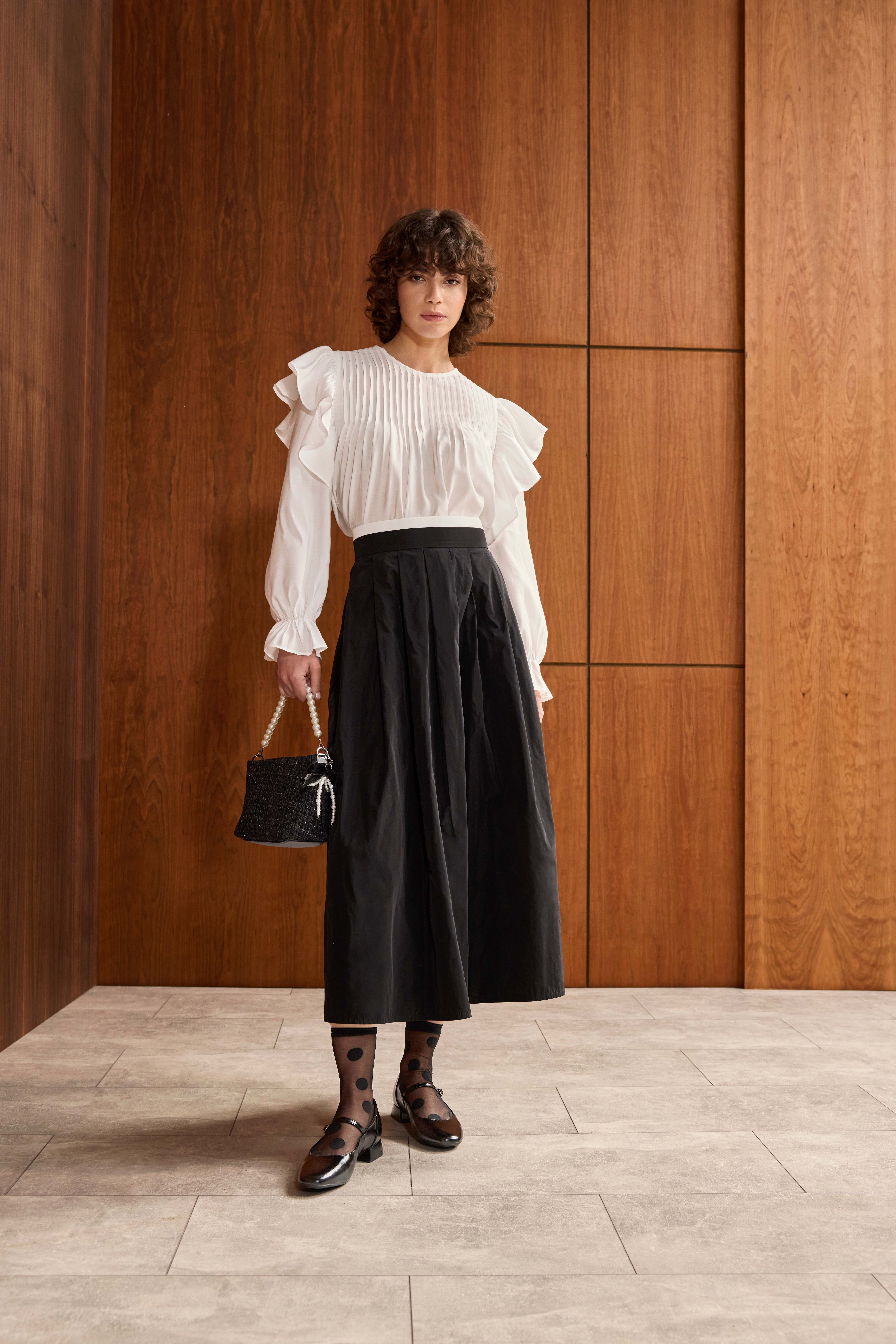 Frau in schlichter Rüschenbluse mit Volants, kombiniert mit schwarzem Midi-Rock und passenden Loafern