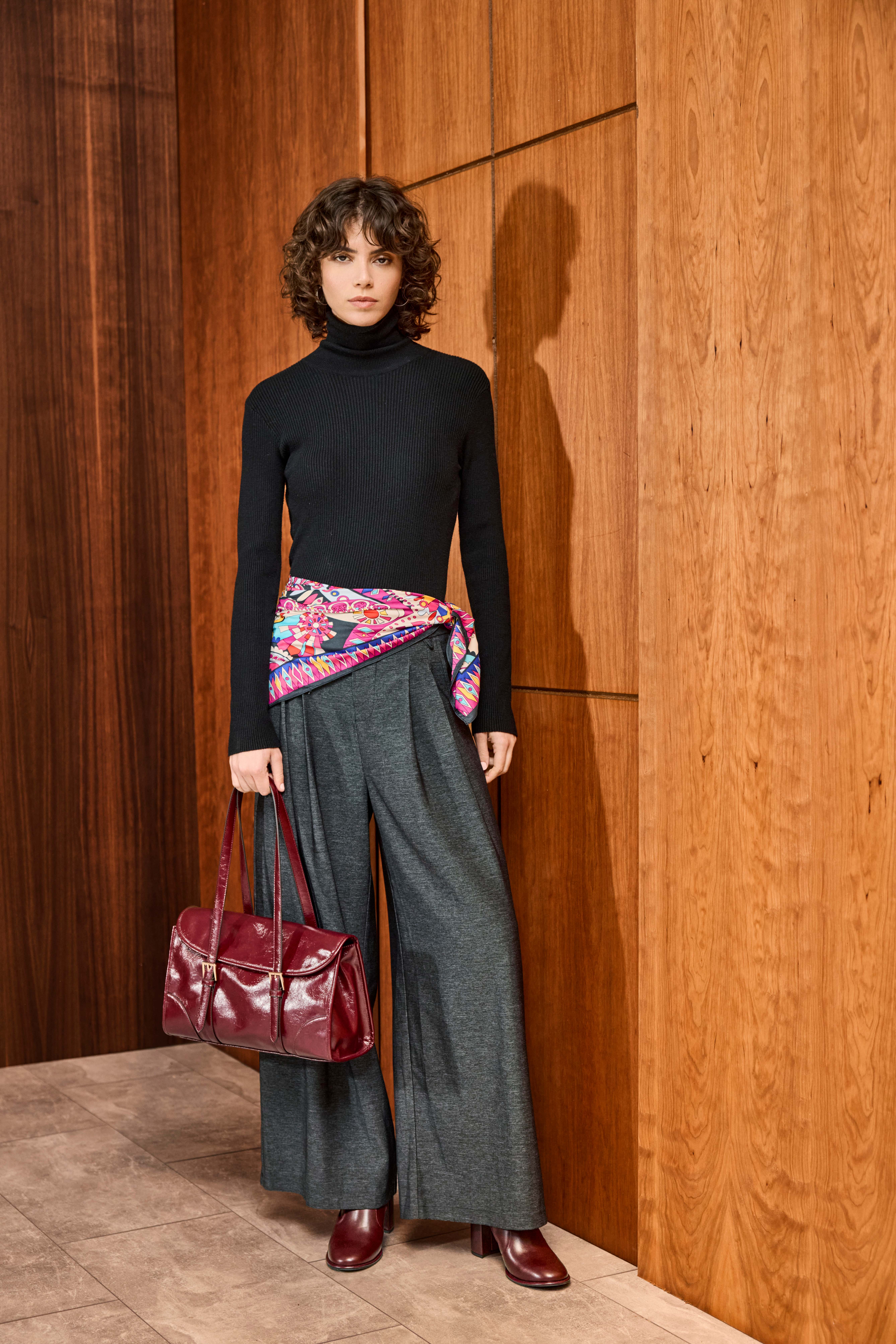 Donna con maglione a collo alto nero, abbinato a pantaloni grigi e un foulard di seta annodato sui fianchi