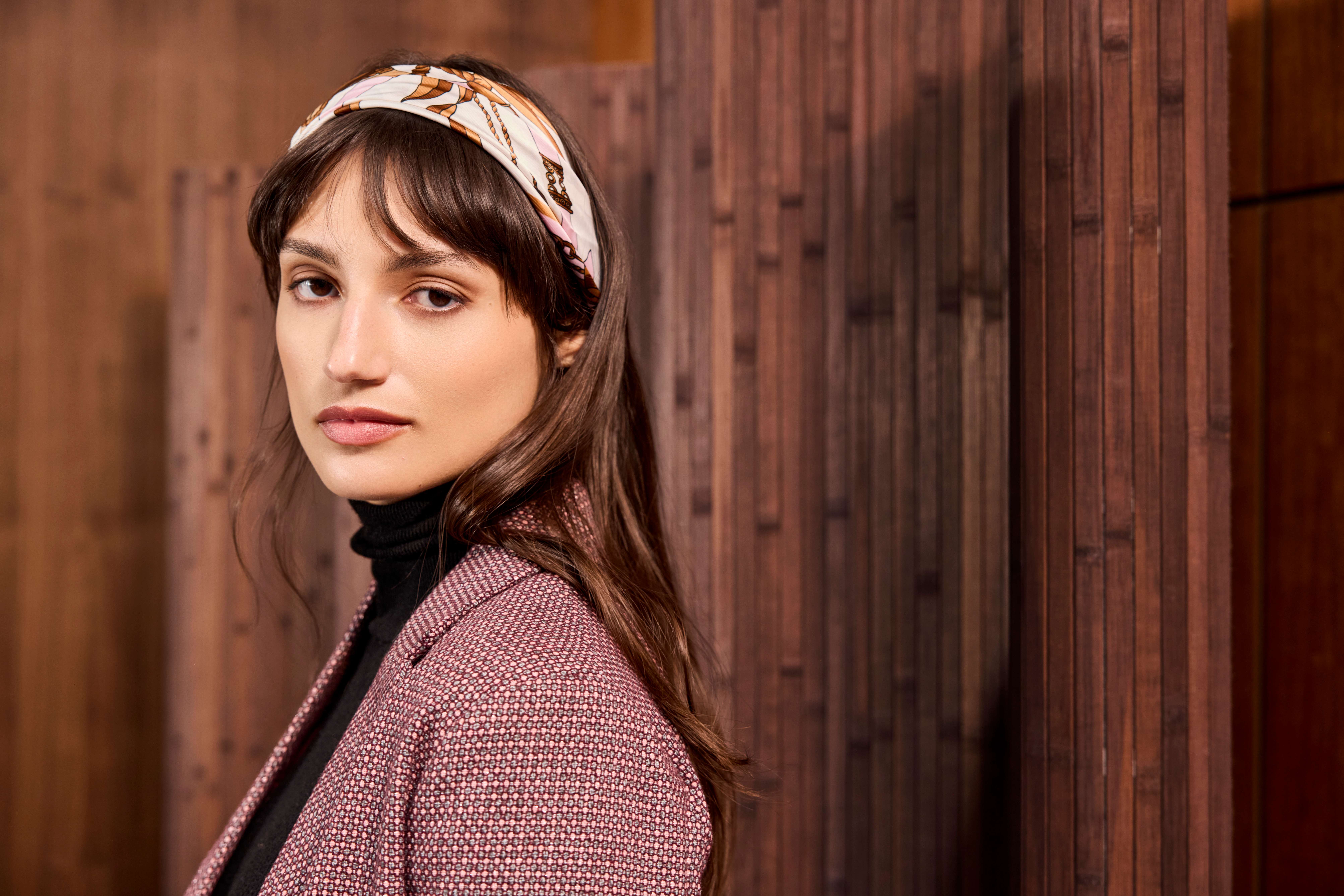 Donna con un foulard tra i capelli, in piedi davanti a una parete di legno
