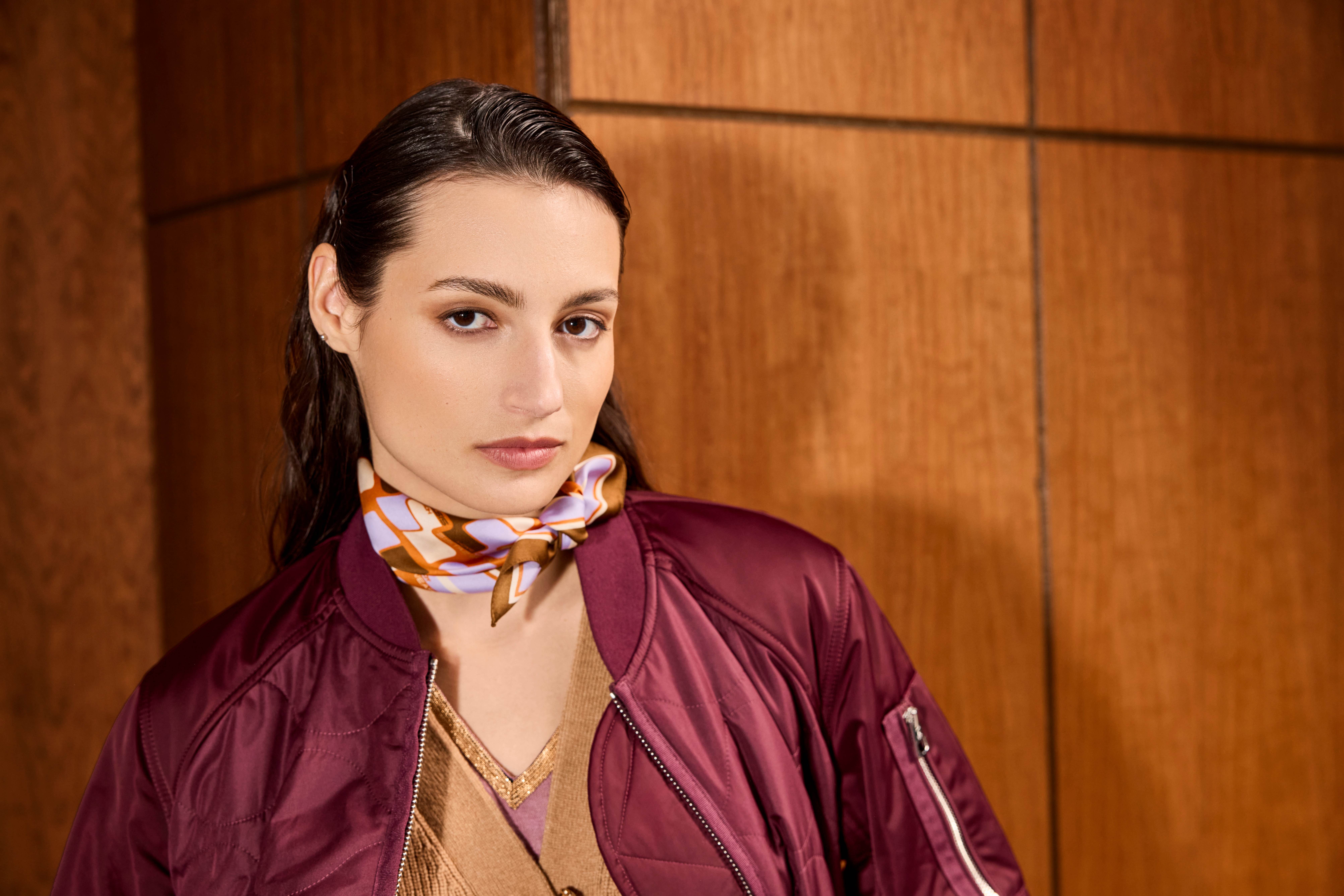 Una donna indossa un foulard di seta colorato, abbinato a un bomber rosso di raso