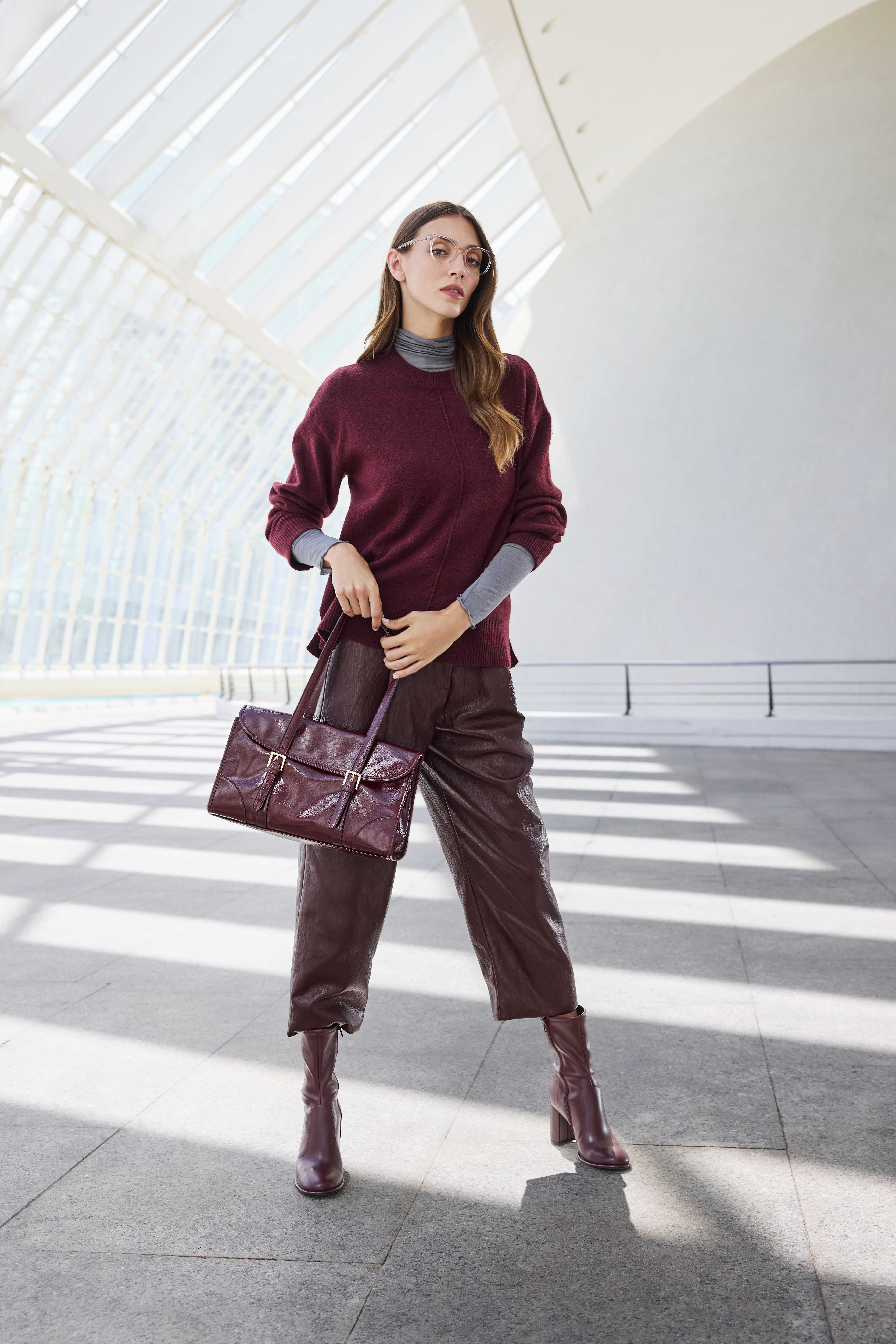 Eine Frau trägt ein burgunderrotes Outfit mit Lederhose, passender Tasche und Absatzstiefeletten