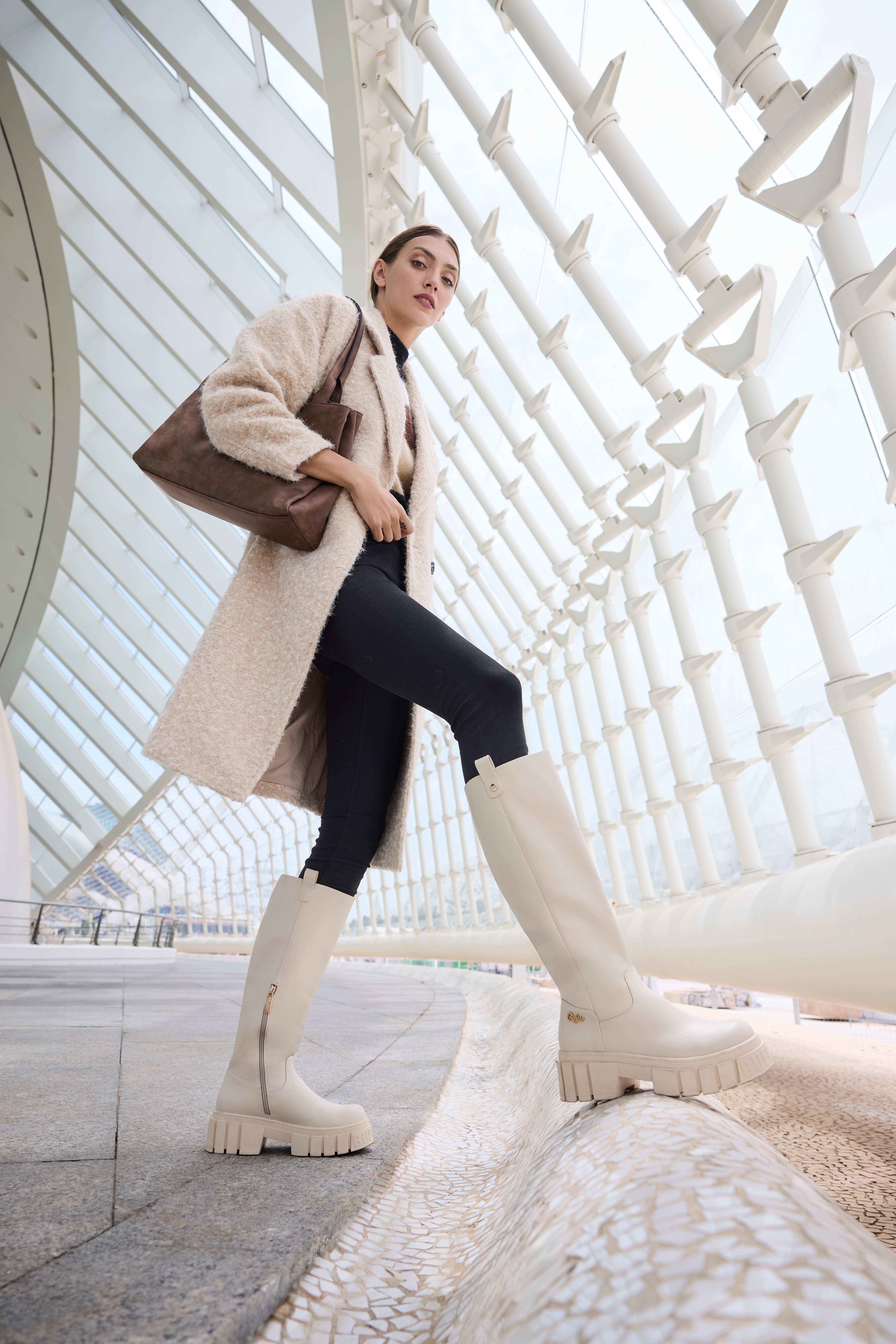 Una donna indossa un cappotto beige, pantaloni neri e stivali beige con zeppa che arrivano sotto il ginocchio