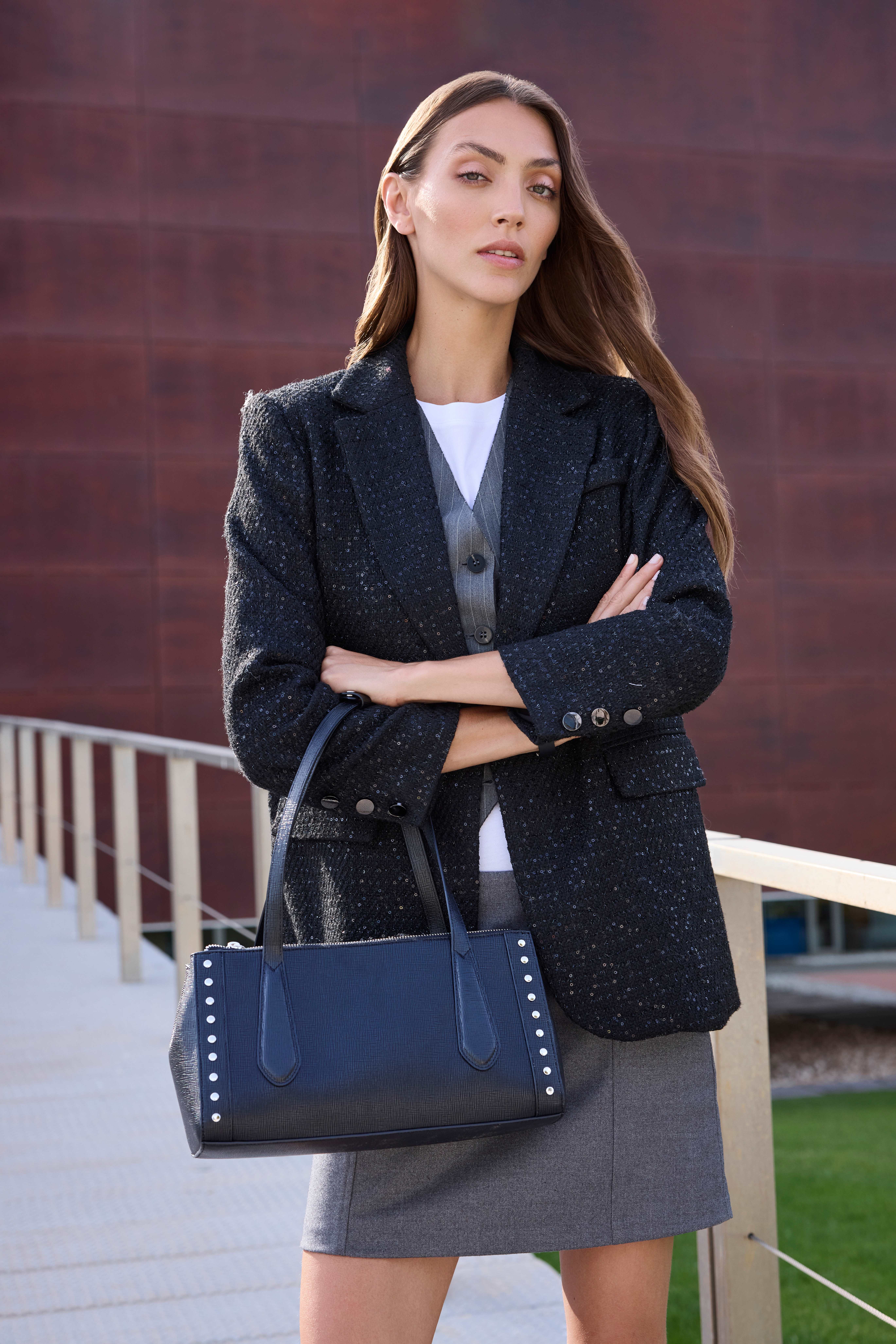 Eine junge Frau trägt einen dunklen Blazer, einen grauen Rock und eine dunkelblaue Tasche