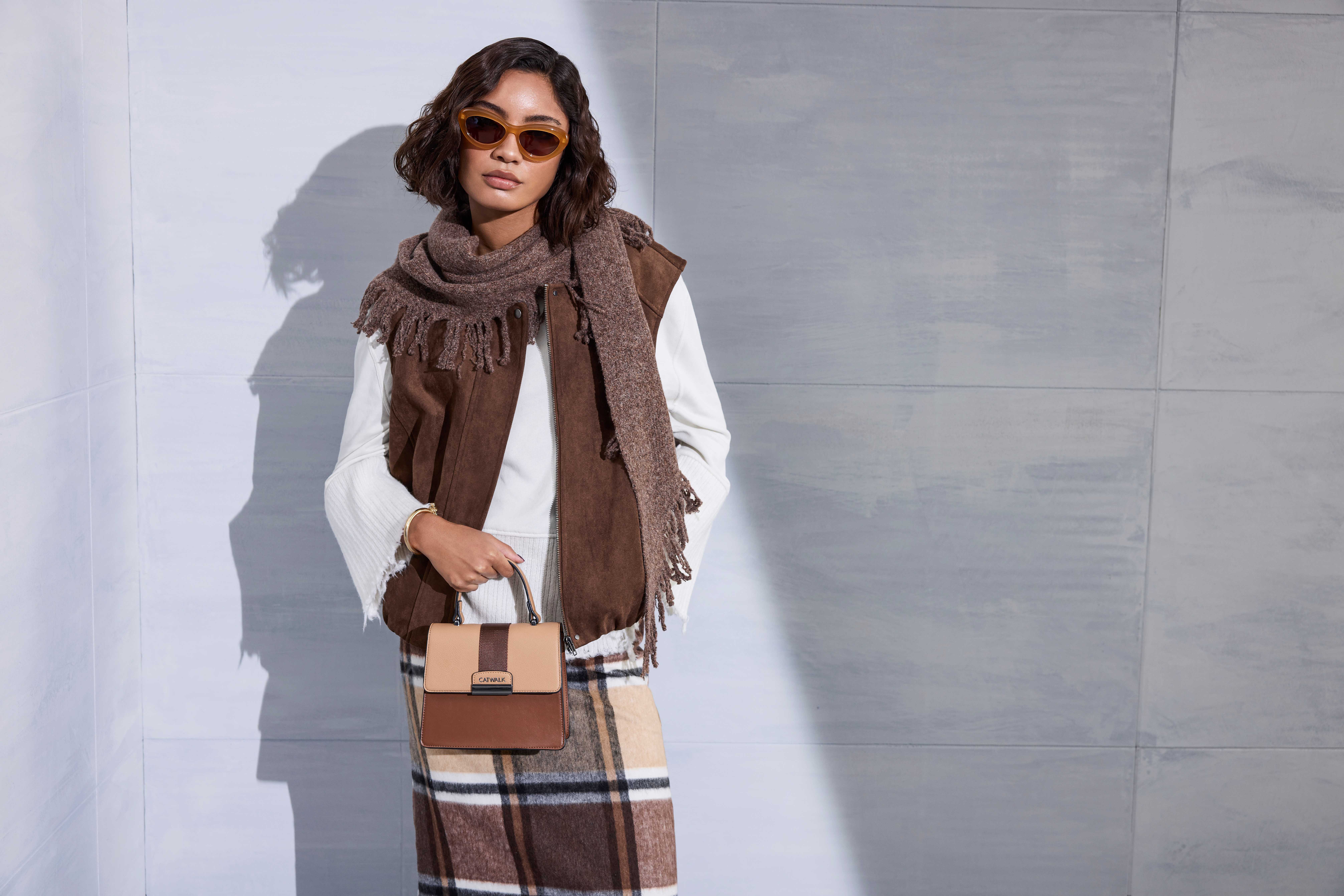 Model in Wildlederweste und Karorock hält zweifarbige Handtasche in Braun und Beige