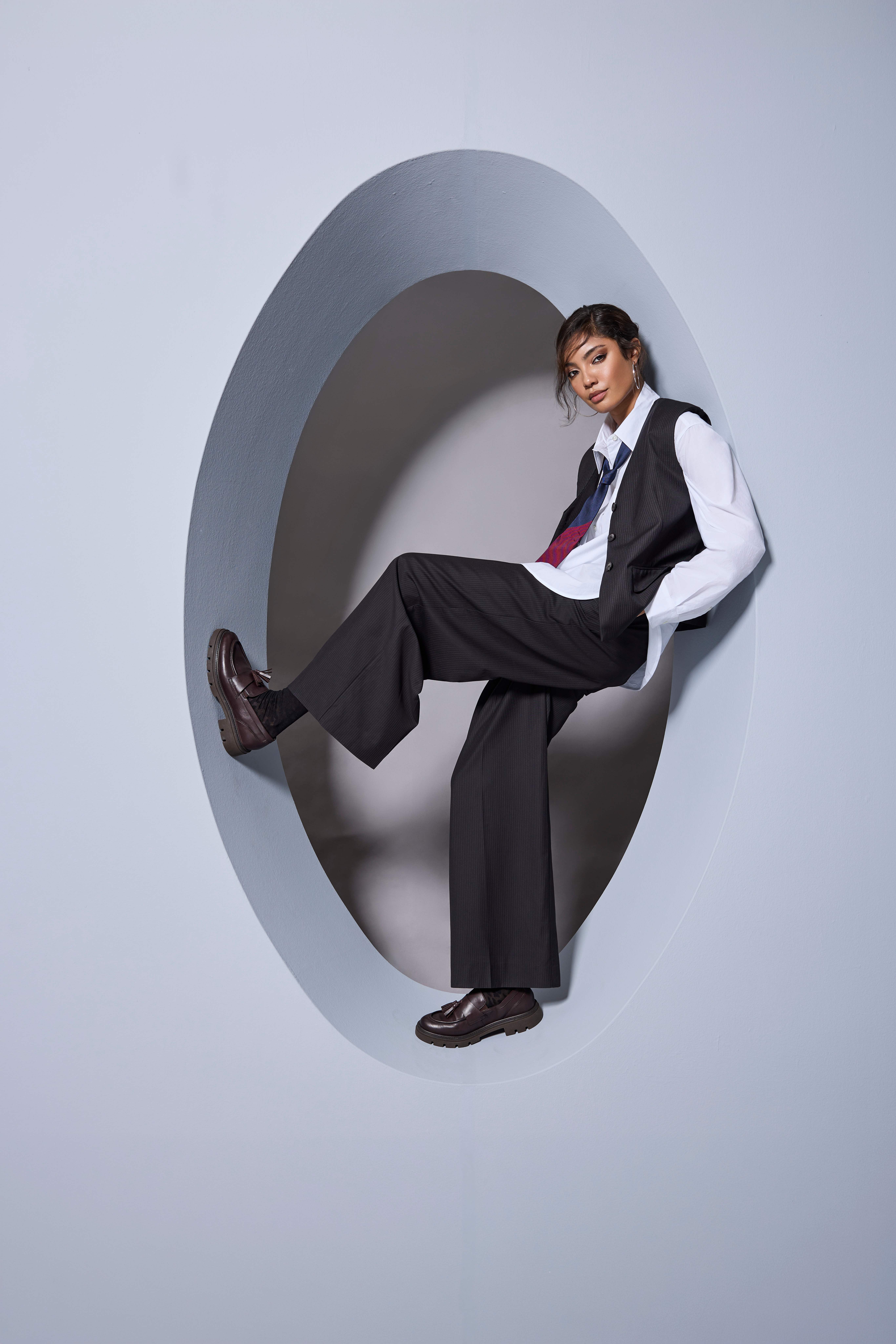 Eine Person in eleganter Office-Kleidung sitzt in einer ovalen Wandöffnung