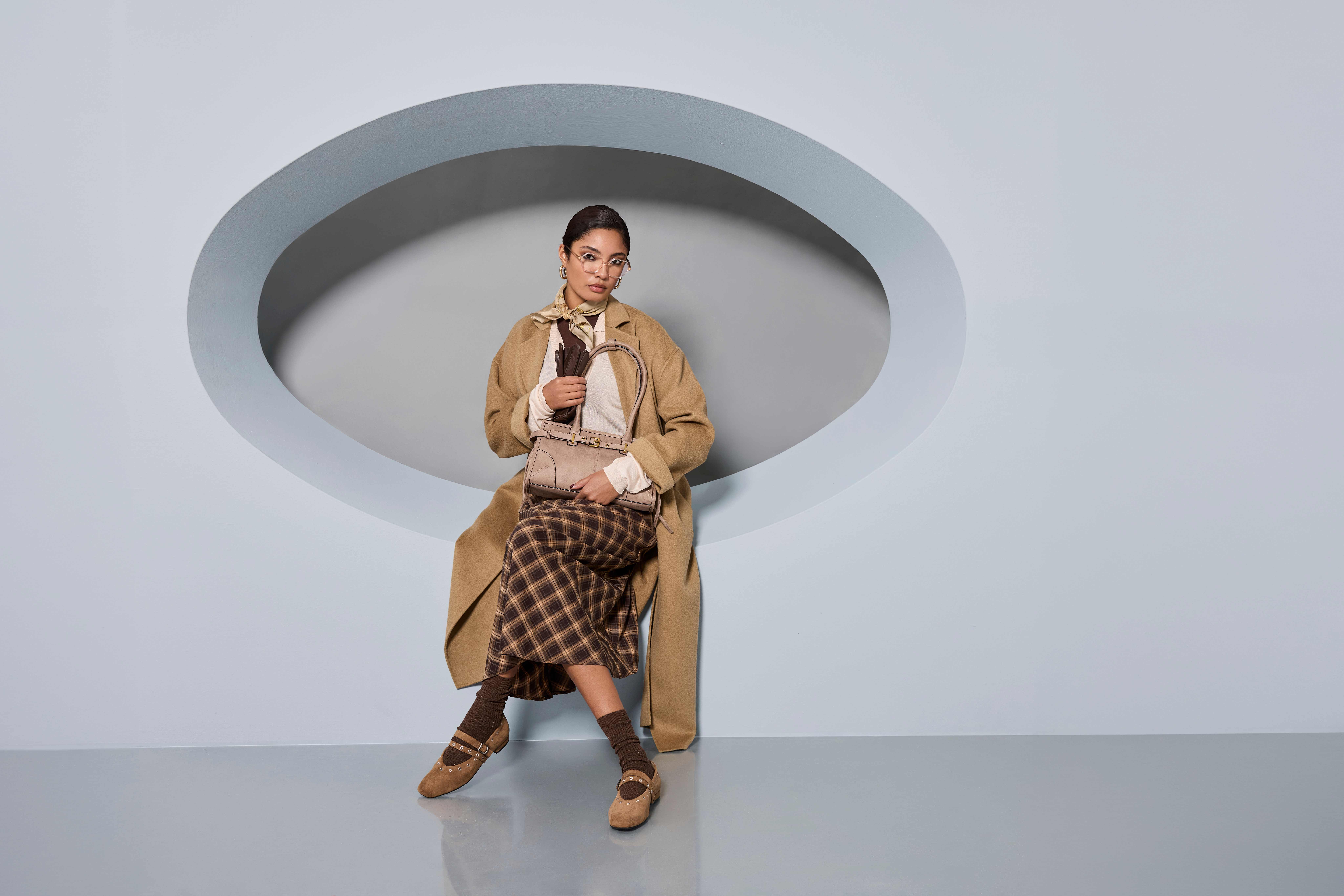 Frau in Layering-Outfit in Braun sitzt in Wand-Ausschnitt