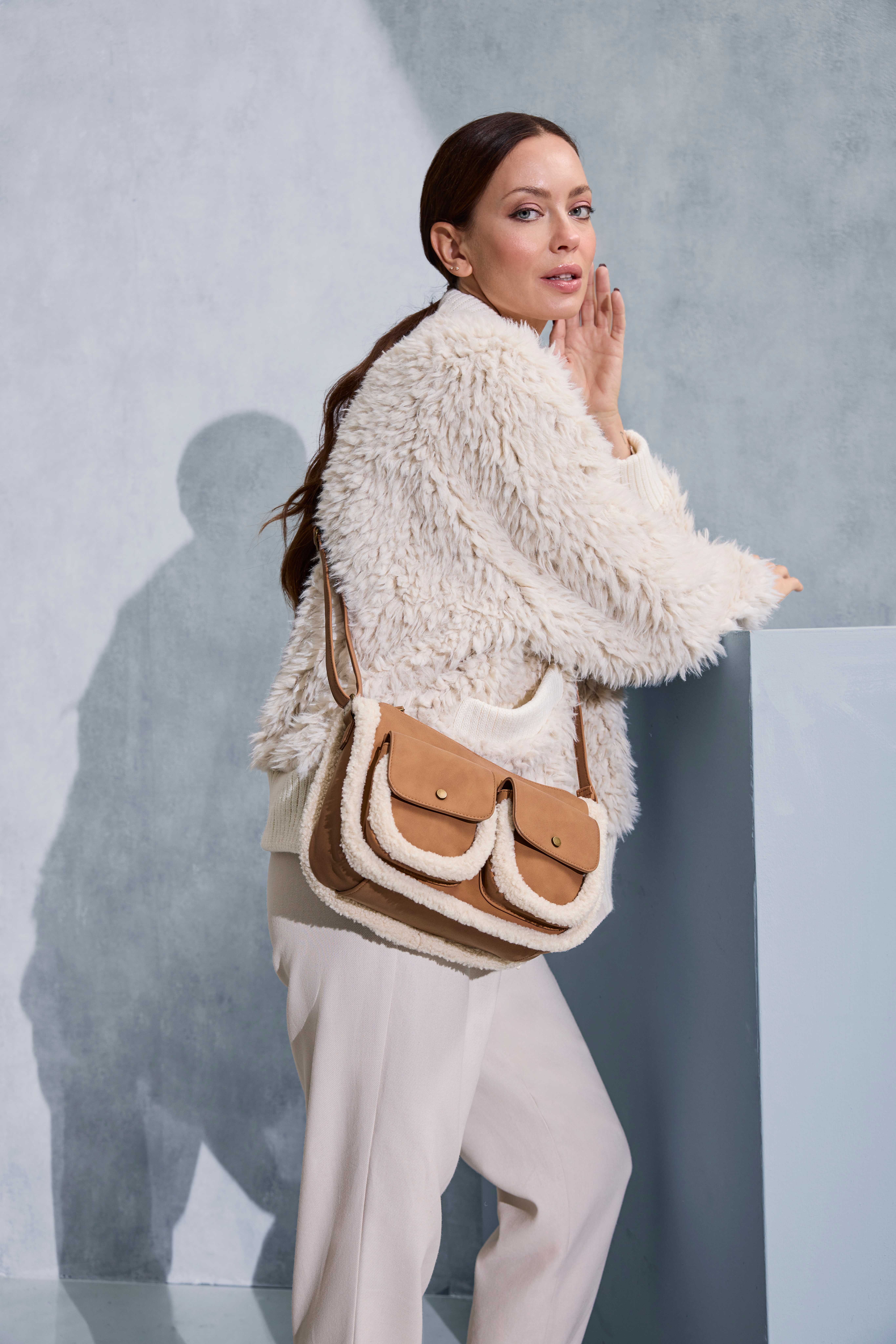 Frau trägt ein komplettes Creme-Outfit mit flauschiger Jacke, creme Hose und brauner Tasche