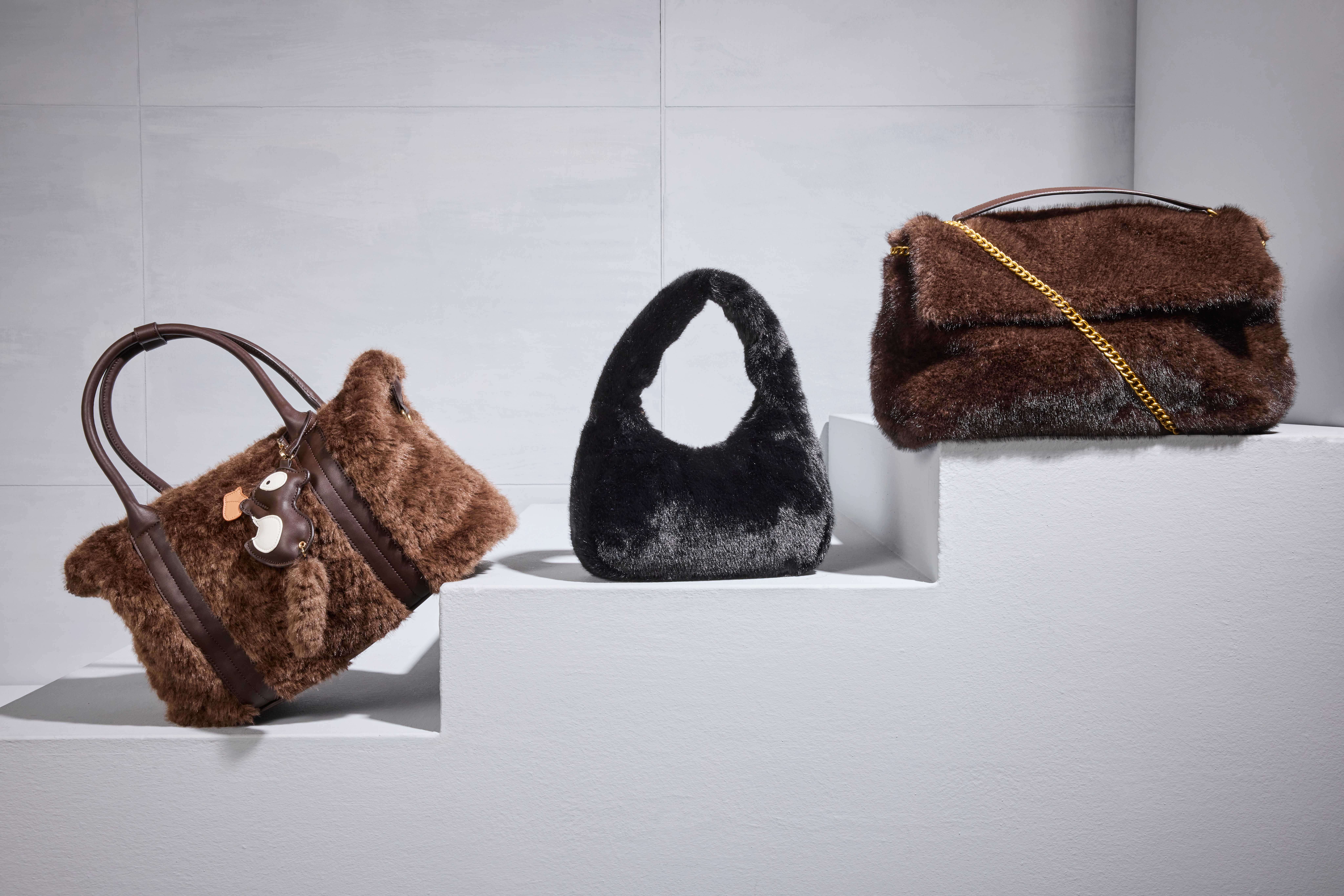 Drei flauschige Handtaschen in Braun und Schwarz auf weißen Podesten.