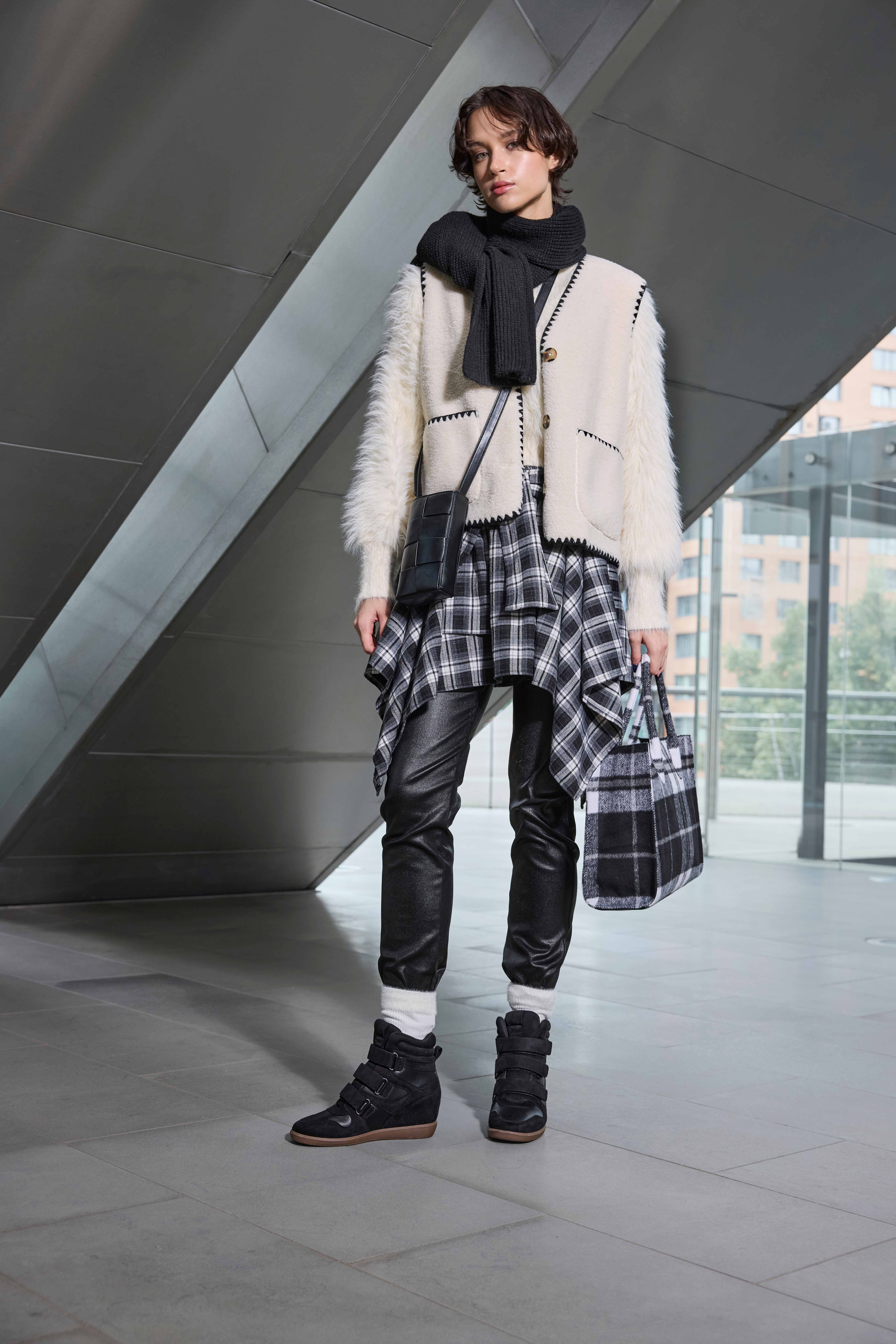 Frau mit heller Strickjacke, Karorock und Lederhose im Layering-Stil