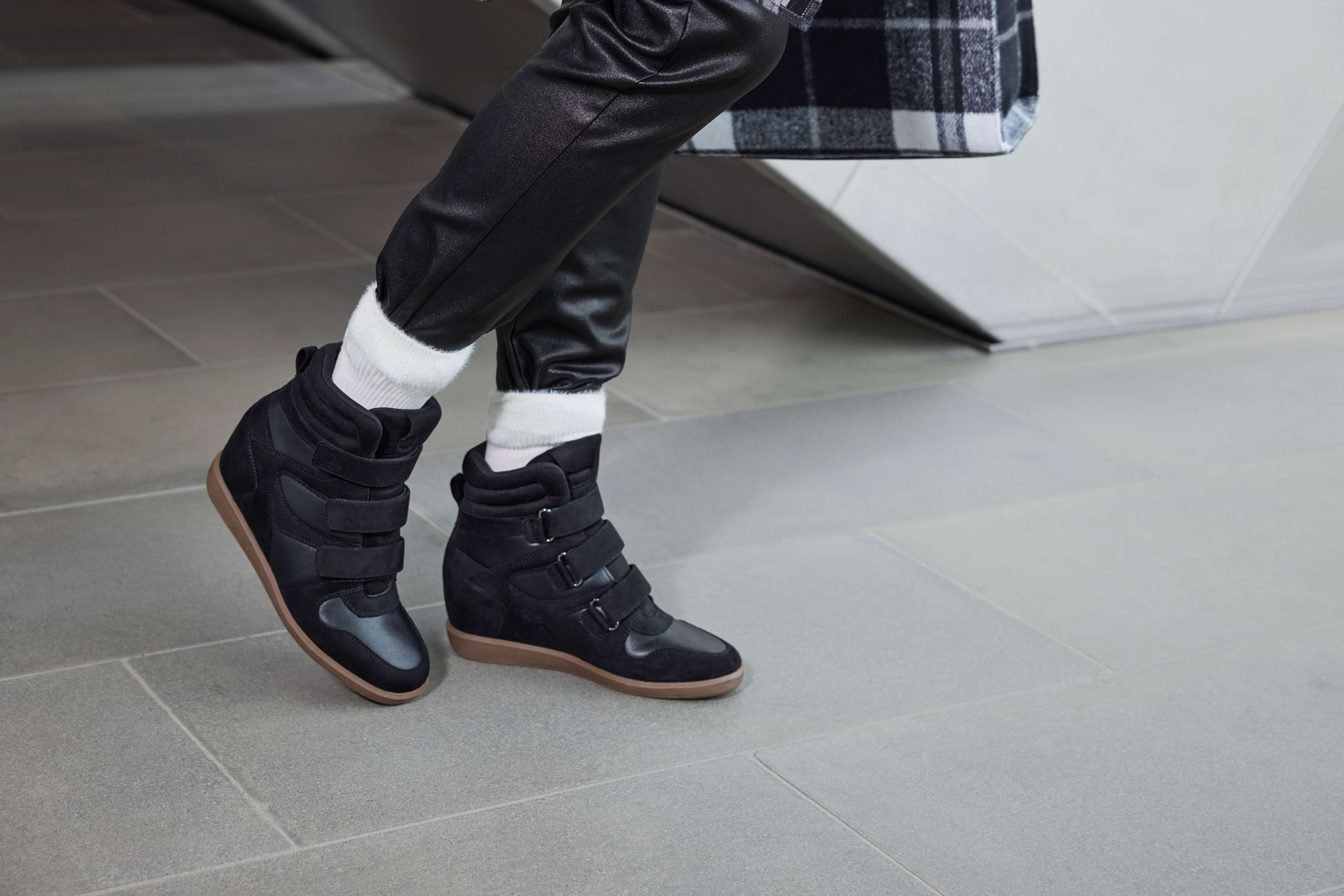 Schwarze High-Top-Sneaker mit mehreren Klettverschlüssen und brauner Sohle, kombiniert mit weißen Socken und schwarzer Hose.