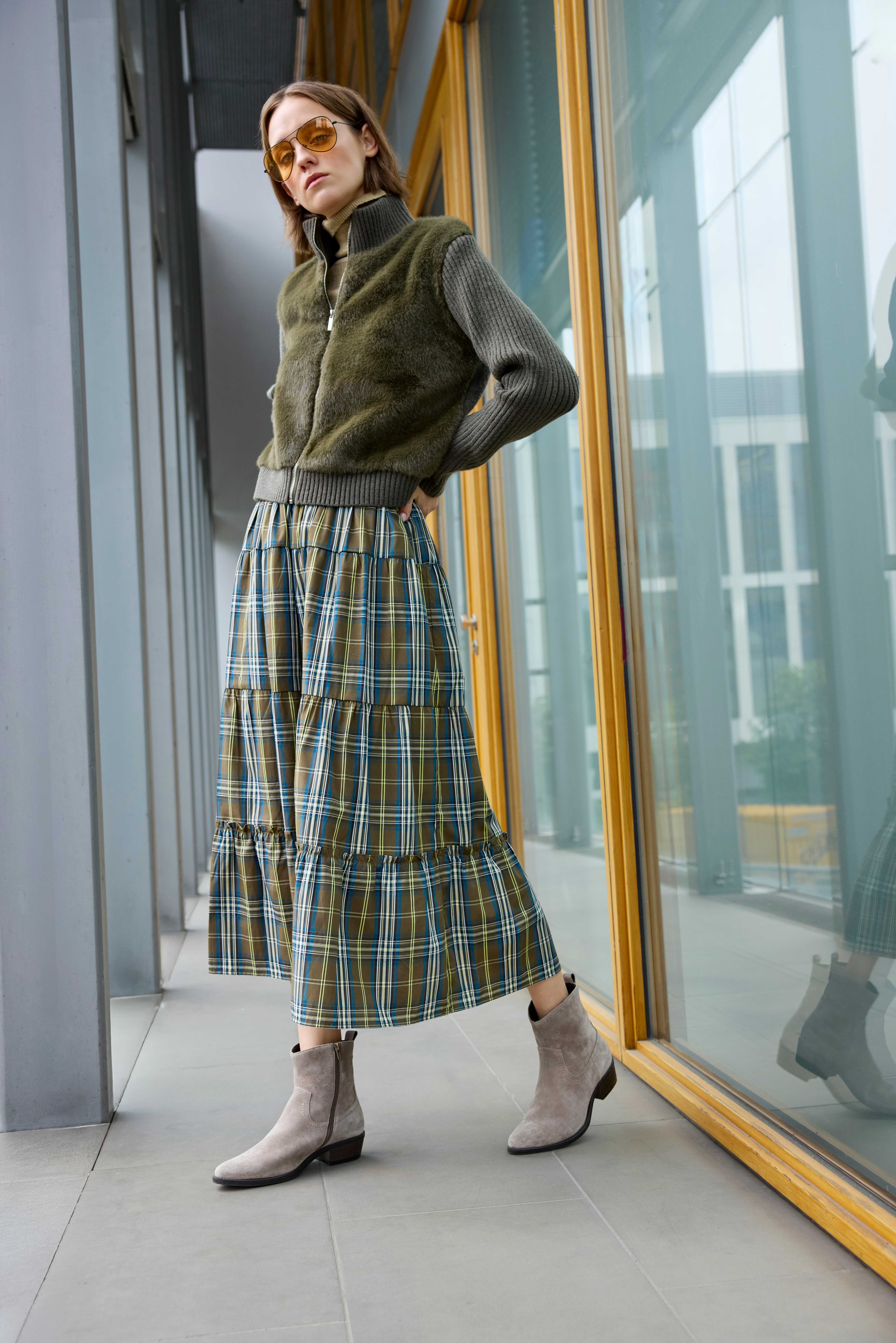 Eine Frau mit grauen Western Boots, grün-blauem Rock und grüner Jacke