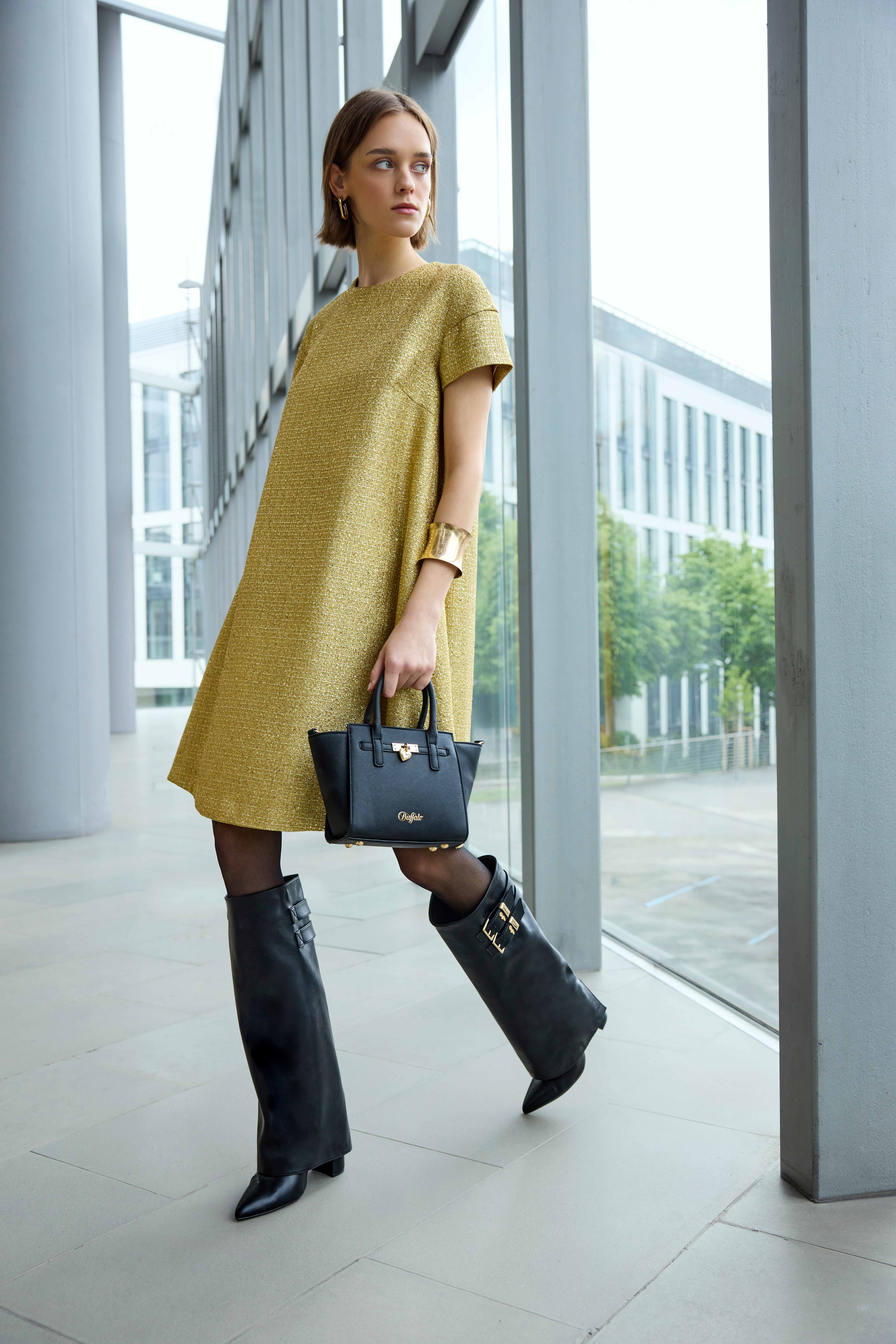 Frau im goldenen Lurex-Kleid kombiniert schwarze Shark Boots mit Umschlagschaft und kleine Handtasche