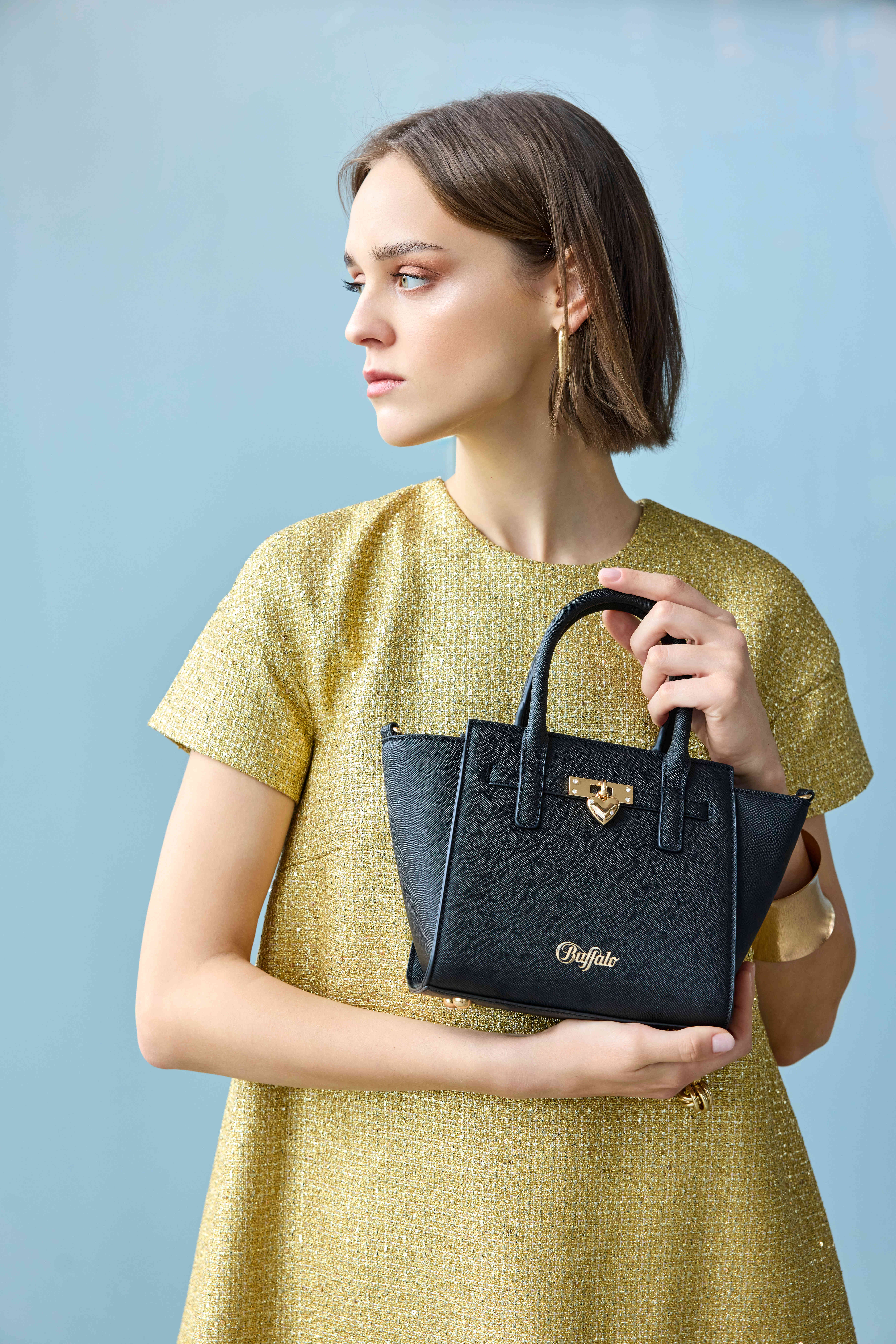 Model im goldenen Tweed-Kleid hält schwarze Buffalo-Handtasche mit Goldschloss