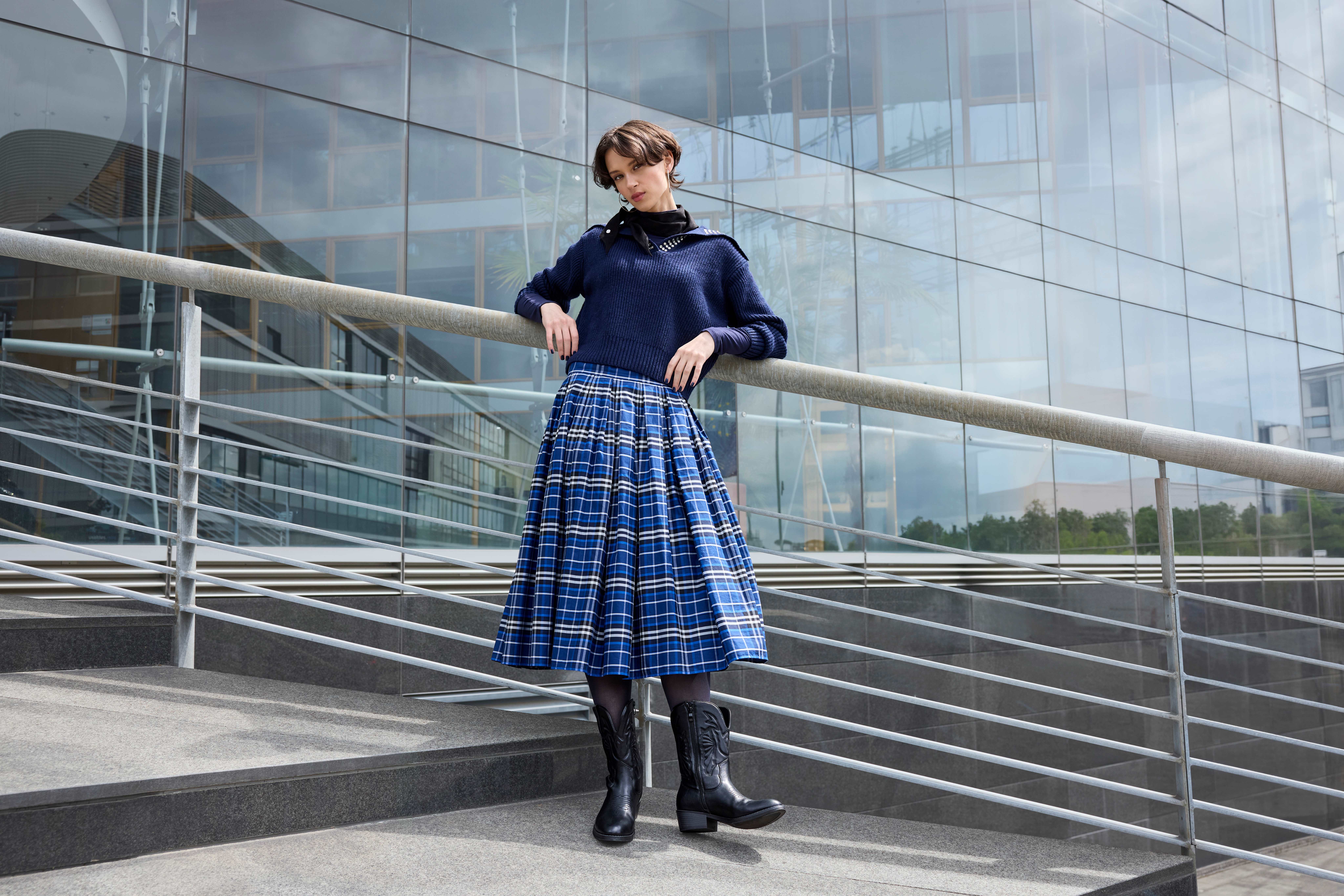 Eine Frau posiert an Geländer in blauen Rock und schwarzen Western Boots