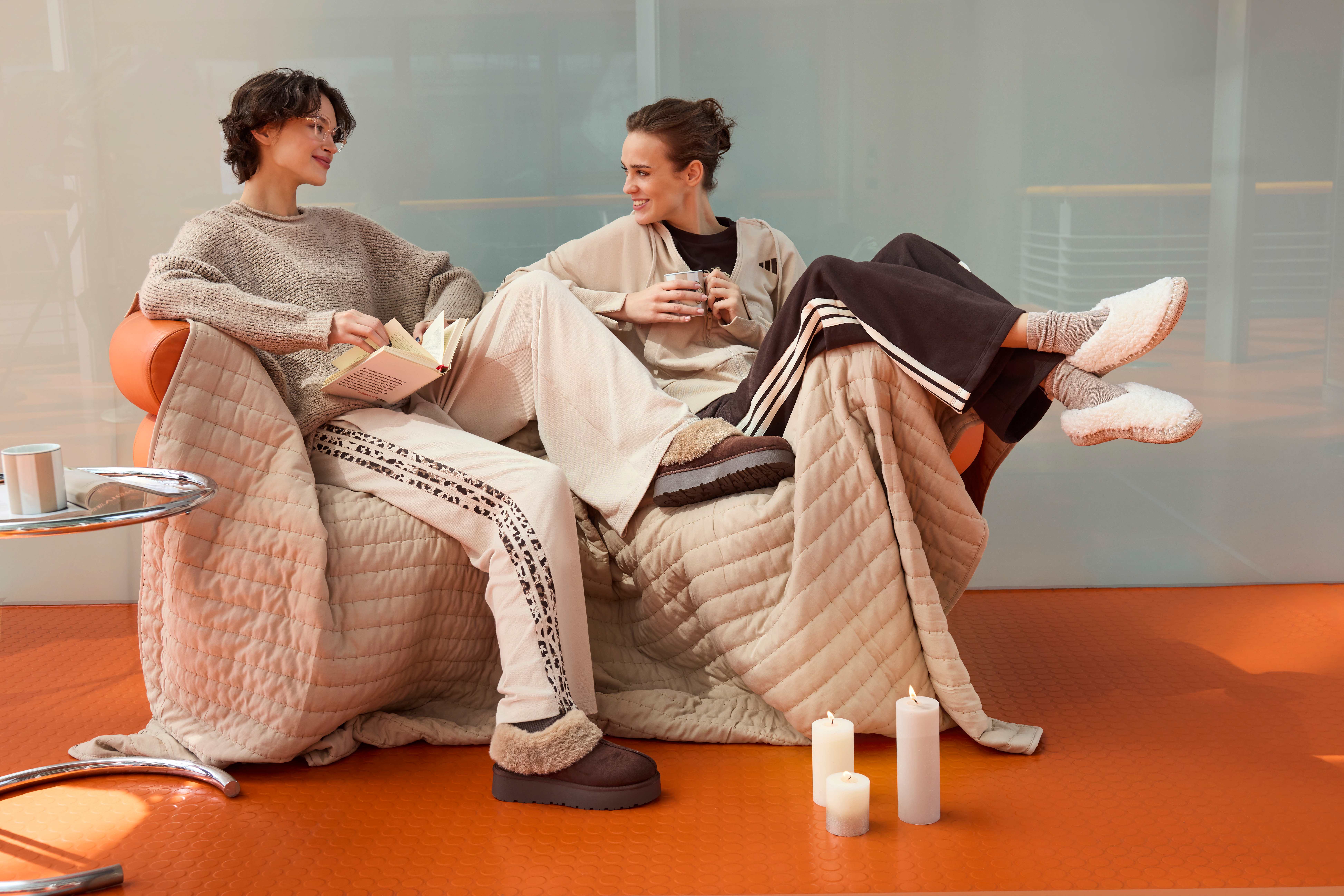 Zwei Frauen sitzen auf einer gemütlichen Couch und tragen bequeme Loungewear in Naturtönen