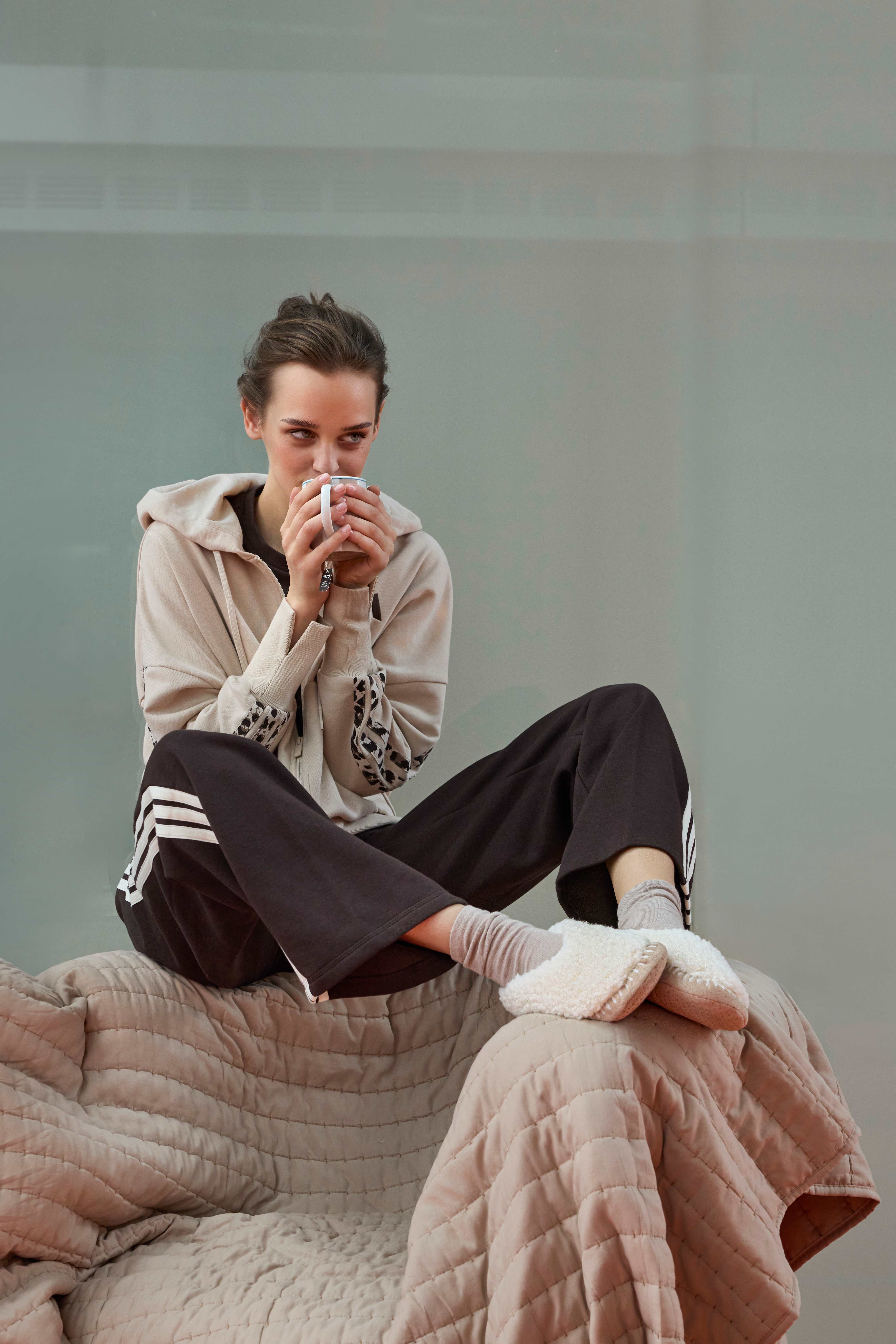 Frau trägt beige Jacke, schwarze Jogginghose mit weißen Streifen und beige Pantoffeln