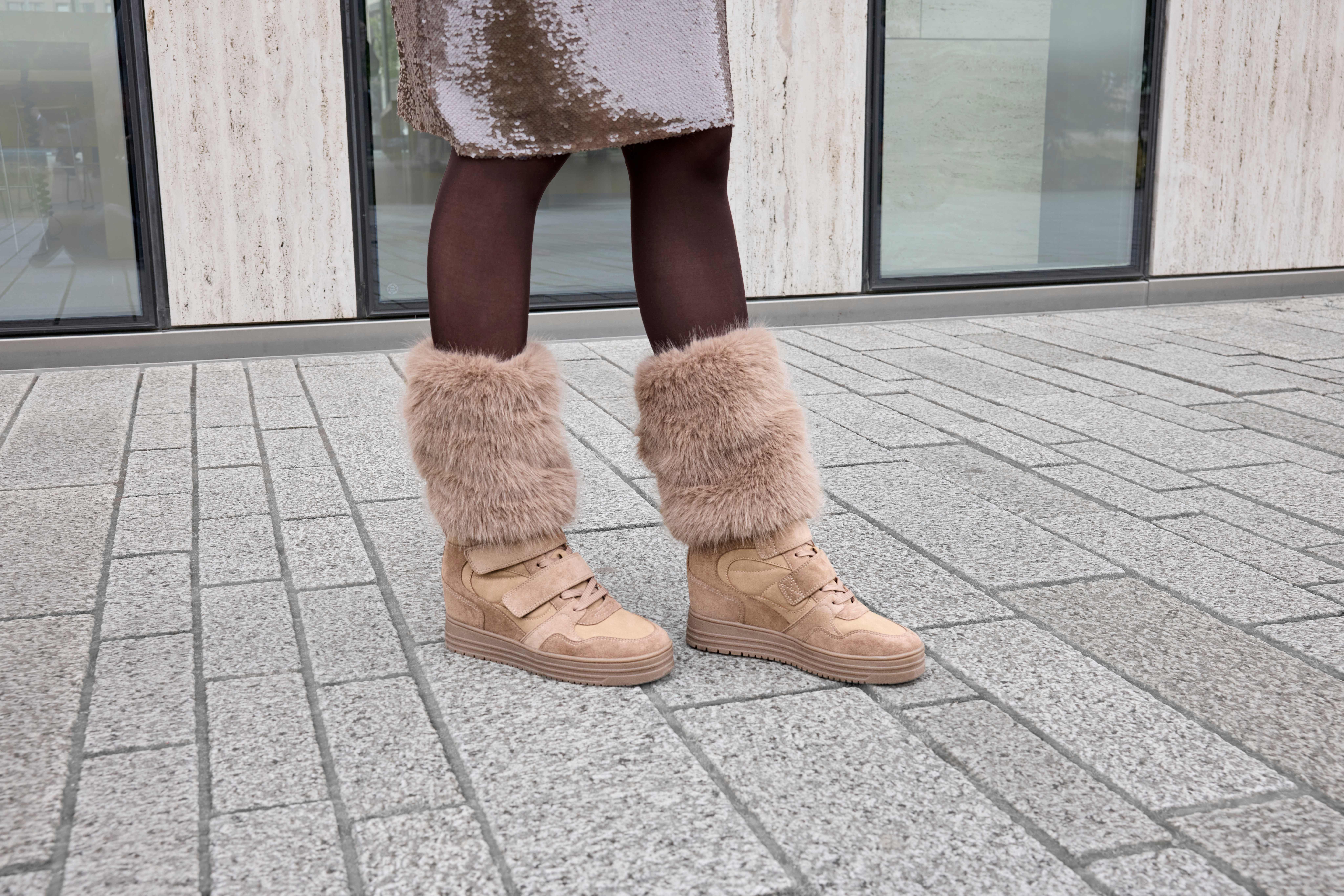 Beige High-Top-Sneaker mit Keilsohle und auffälligem Kunstfellbesatz, kombiniert mit einer dunklen Strumpfhose und einem glitzernden Rock.