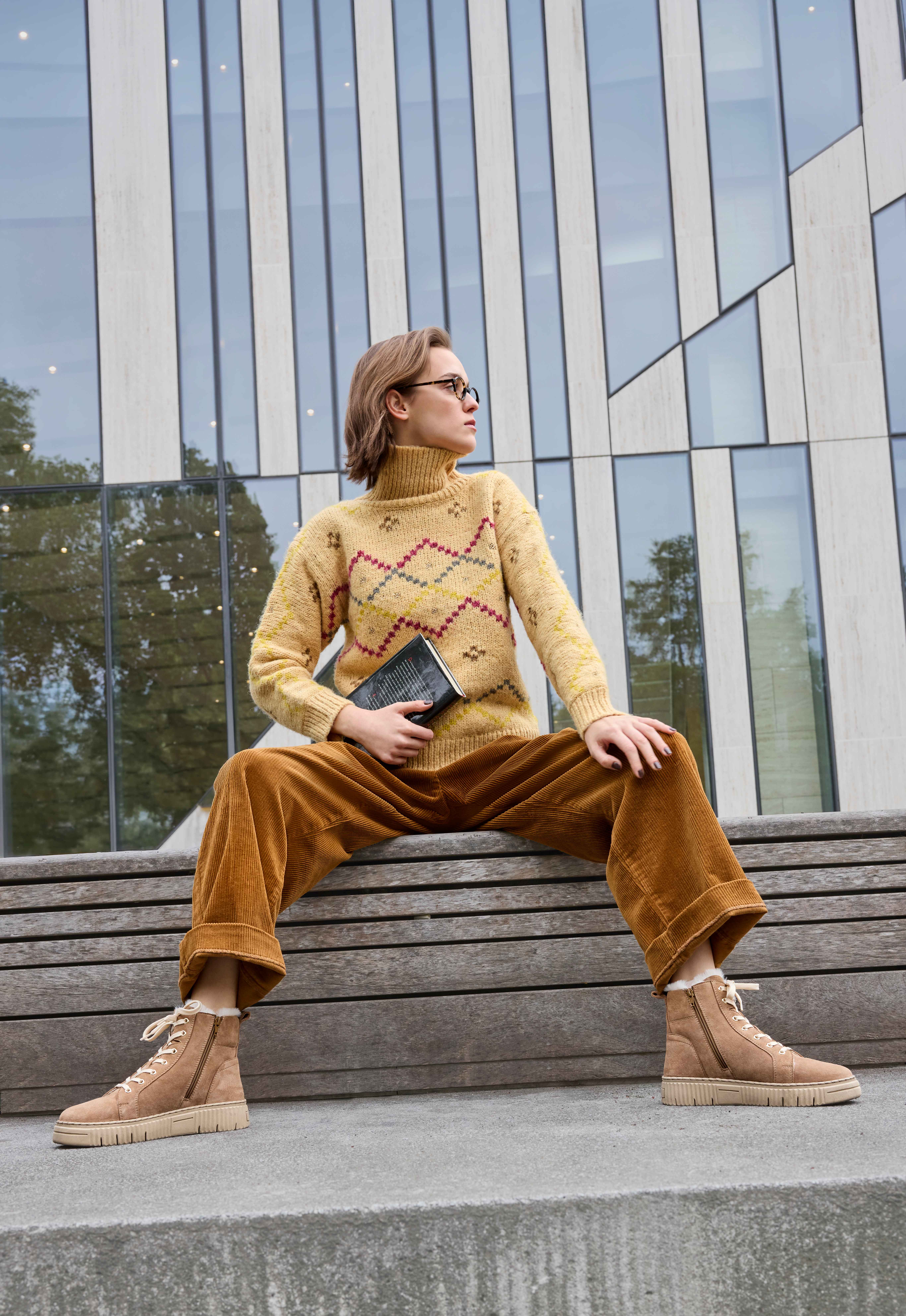 Frau trägt Retro-Outfit mit gelbem Strickpullover, kombiniert mit orange-brauner Hose